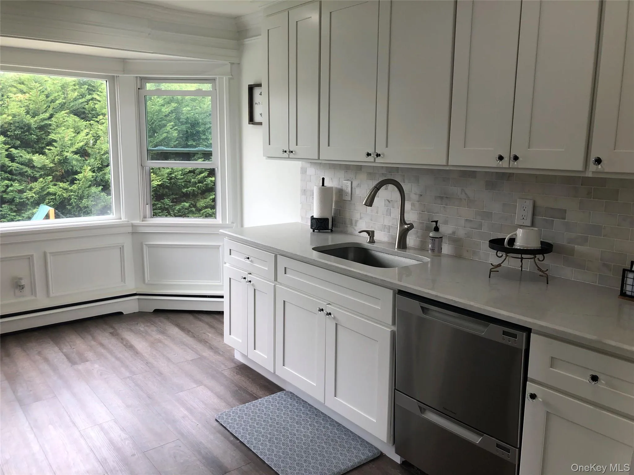 Kitchen with stainless steel dishwasher, white cabinets, light stone counters, and dark wood-style flooring Kitchen with stainless steel dishwasher, white cabinets, light stone counters, and dark wood-style flooring