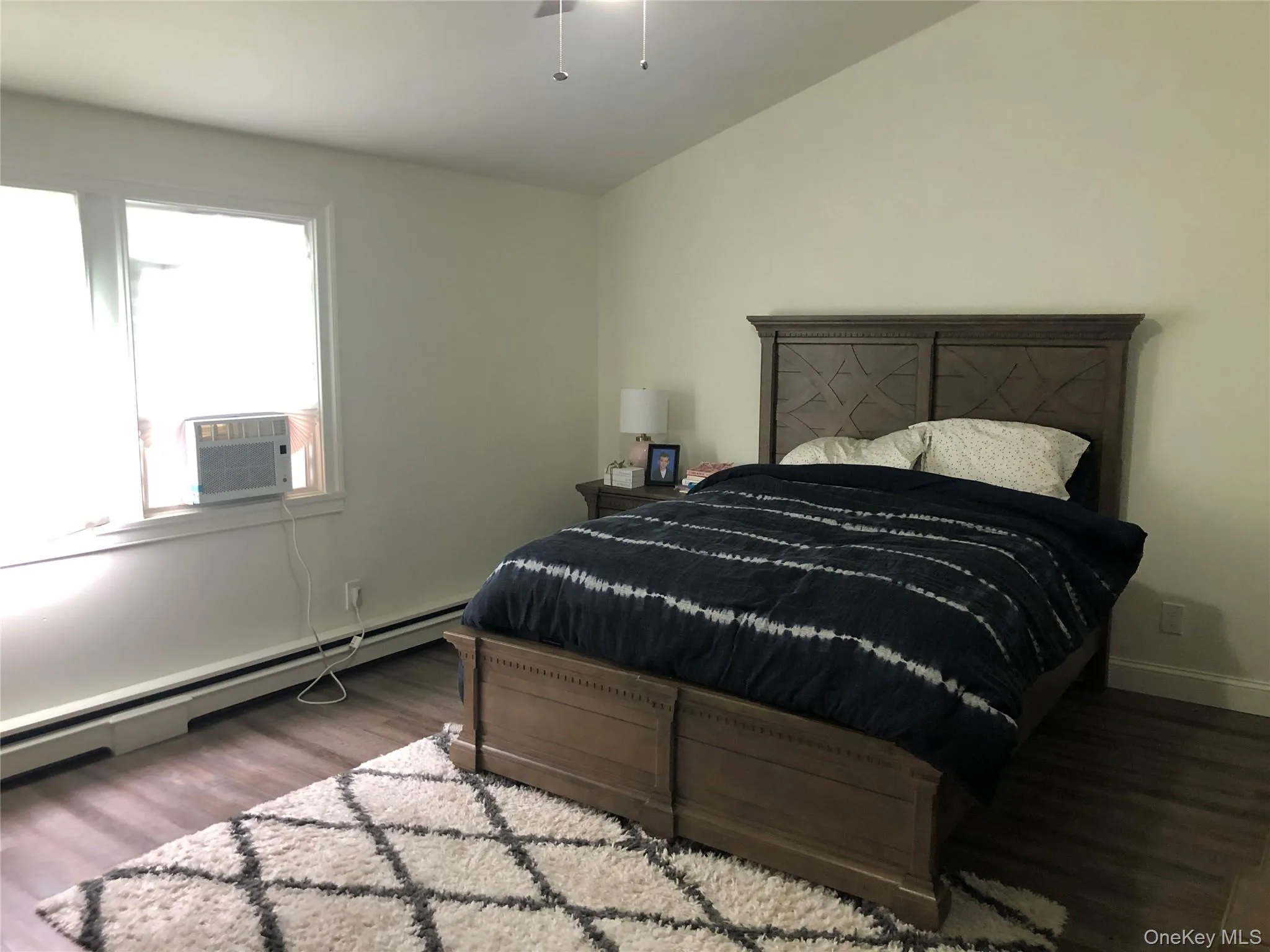 Bedroom with lofted ceiling, a baseboard radiator, dark wood-style floors, and cooling unit Bedroom with lofted ceiling, a baseboard radiator, dark wood-style floors, and cooling unit