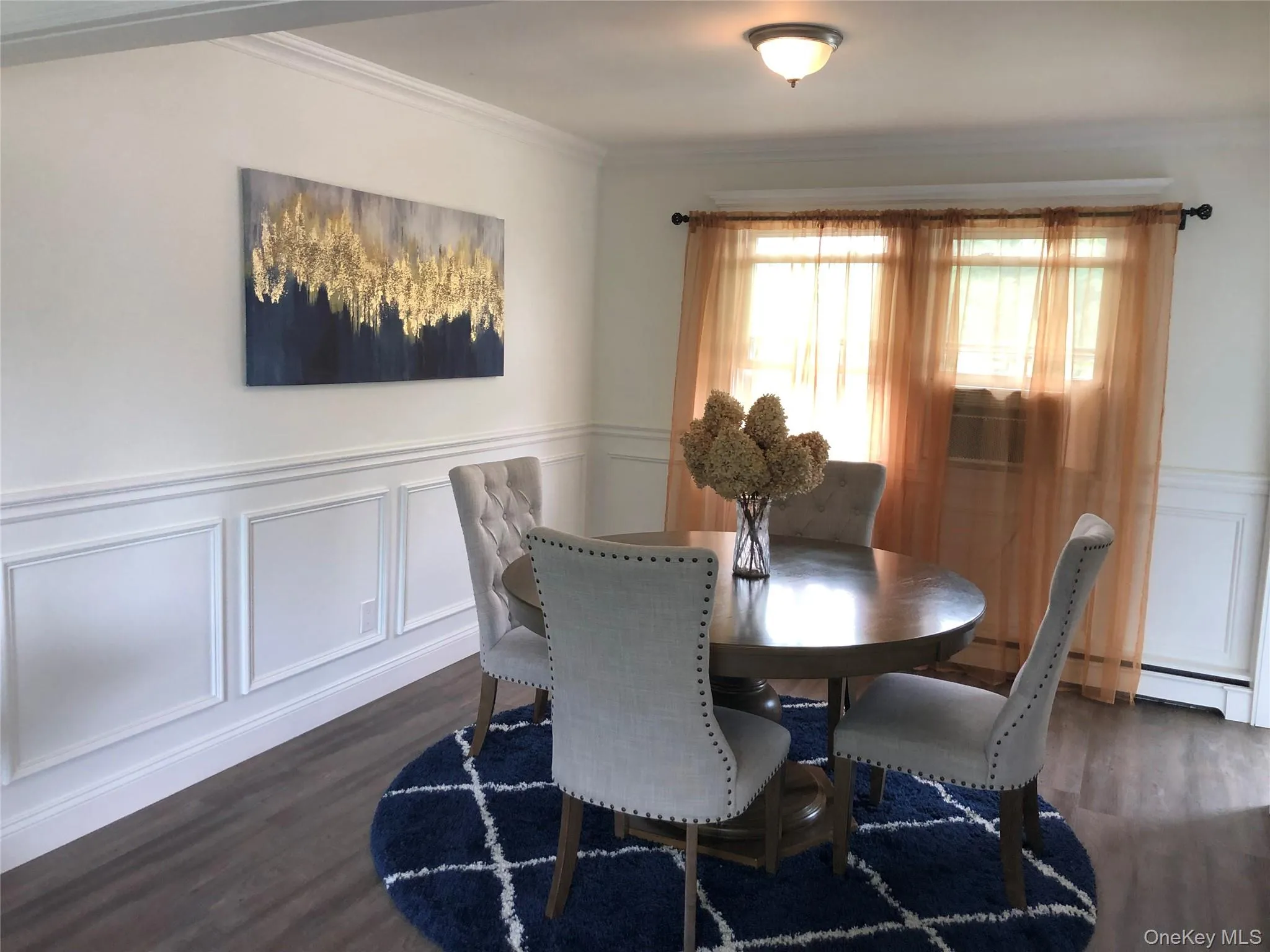 Dining area with a wainscoted wall, a decorative wall, dark wood-style flooring, ornamental molding, and a baseboard heating unit Dining area with a wainscoted wall, a decorative wall, dark wood-style flooring, ornamental molding, and a baseboard heating unit