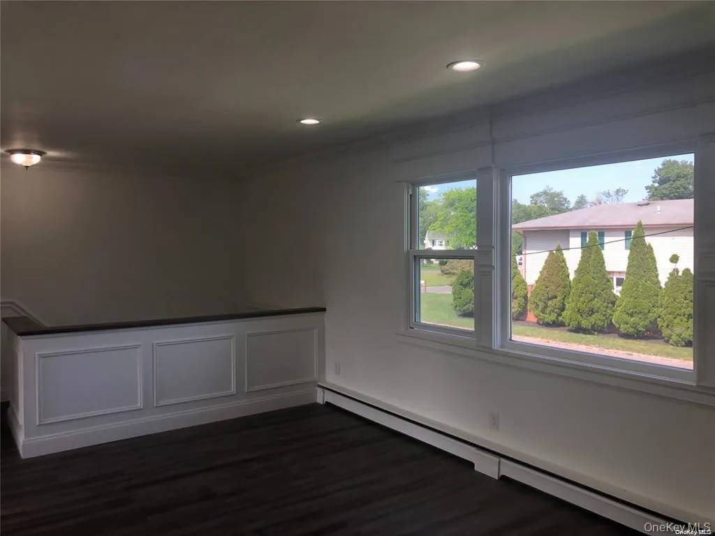 Empty room featuring a baseboard radiator, dark wood-type flooring, recessed lighting, a decorative wall, and crown molding Empty room featuring a baseboard radiator, dark wood-type flooring, recessed lighting, a decorative wall, and crown molding