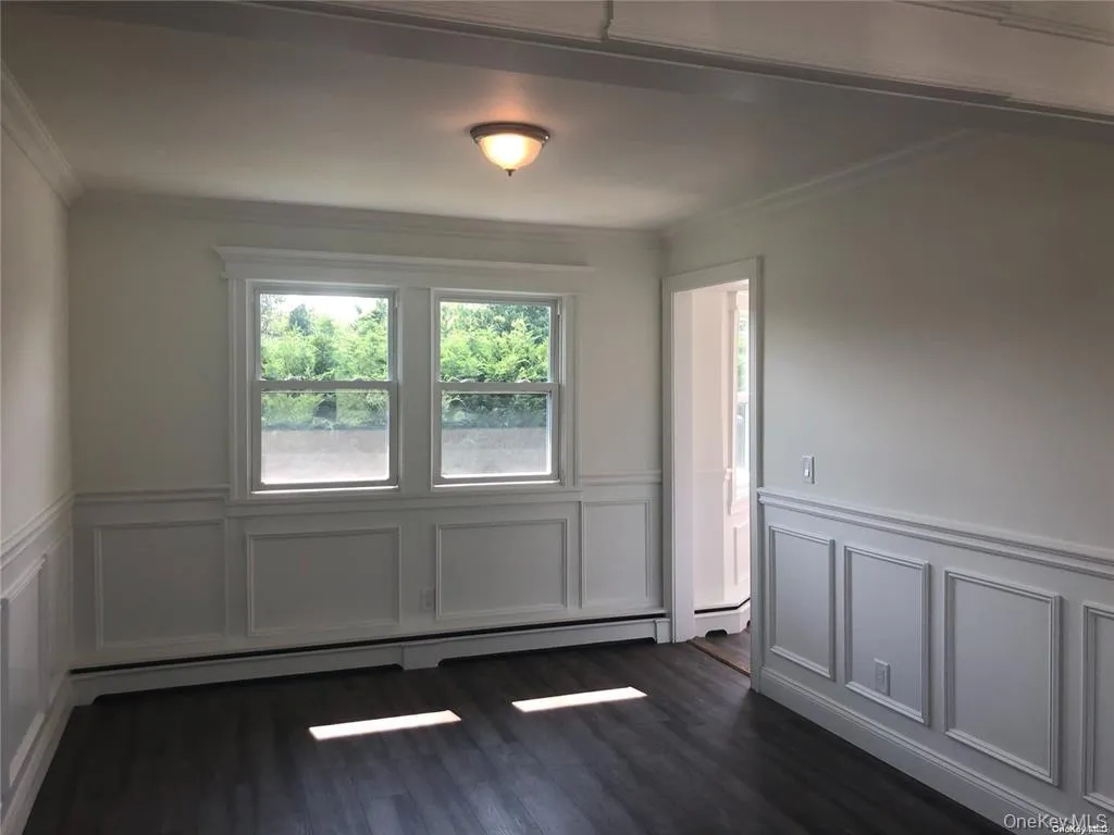 Unfurnished room with ornamental molding, wainscoting, a decorative wall, a baseboard heating unit, and dark wood-style floors Unfurnished room with ornamental molding, wainscoting, a decorative wall, a baseboard heating unit, and dark wood-style floors