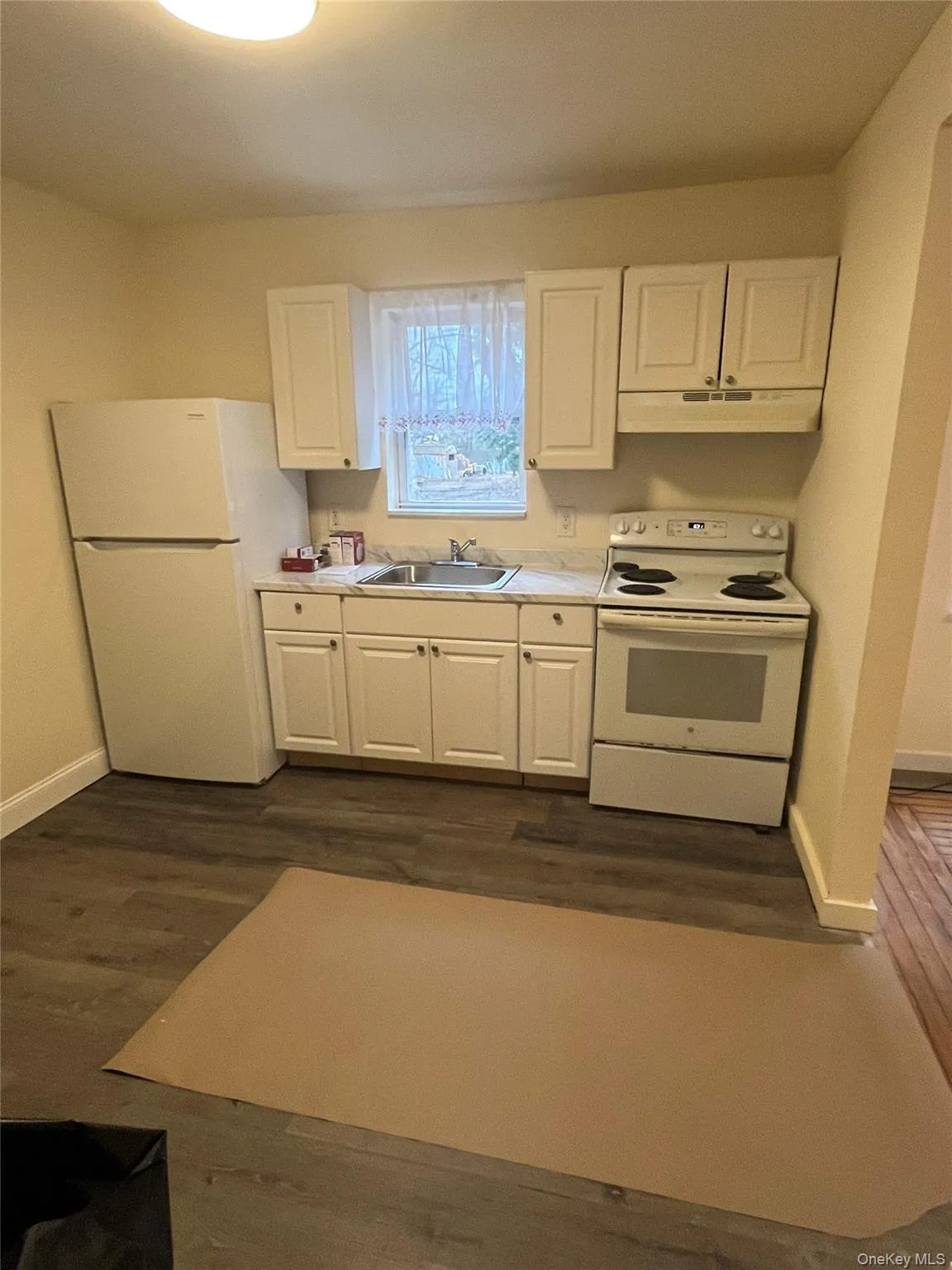 Kitchen with white cabinetry, white appliances, light countertops, and dark wood finished floors Kitchen with white cabinetry, white appliances, light countertops, and dark wood finished floors