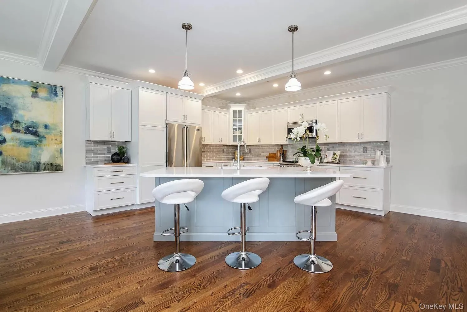 Kitchen with white cabinets, stainless steel appliances, hanging light fixtures, a kitchen island with sink, and crown molding Kitchen with white cabinets, stainless steel appliances, hanging light fixtures, a kitchen island with sink, and crown molding