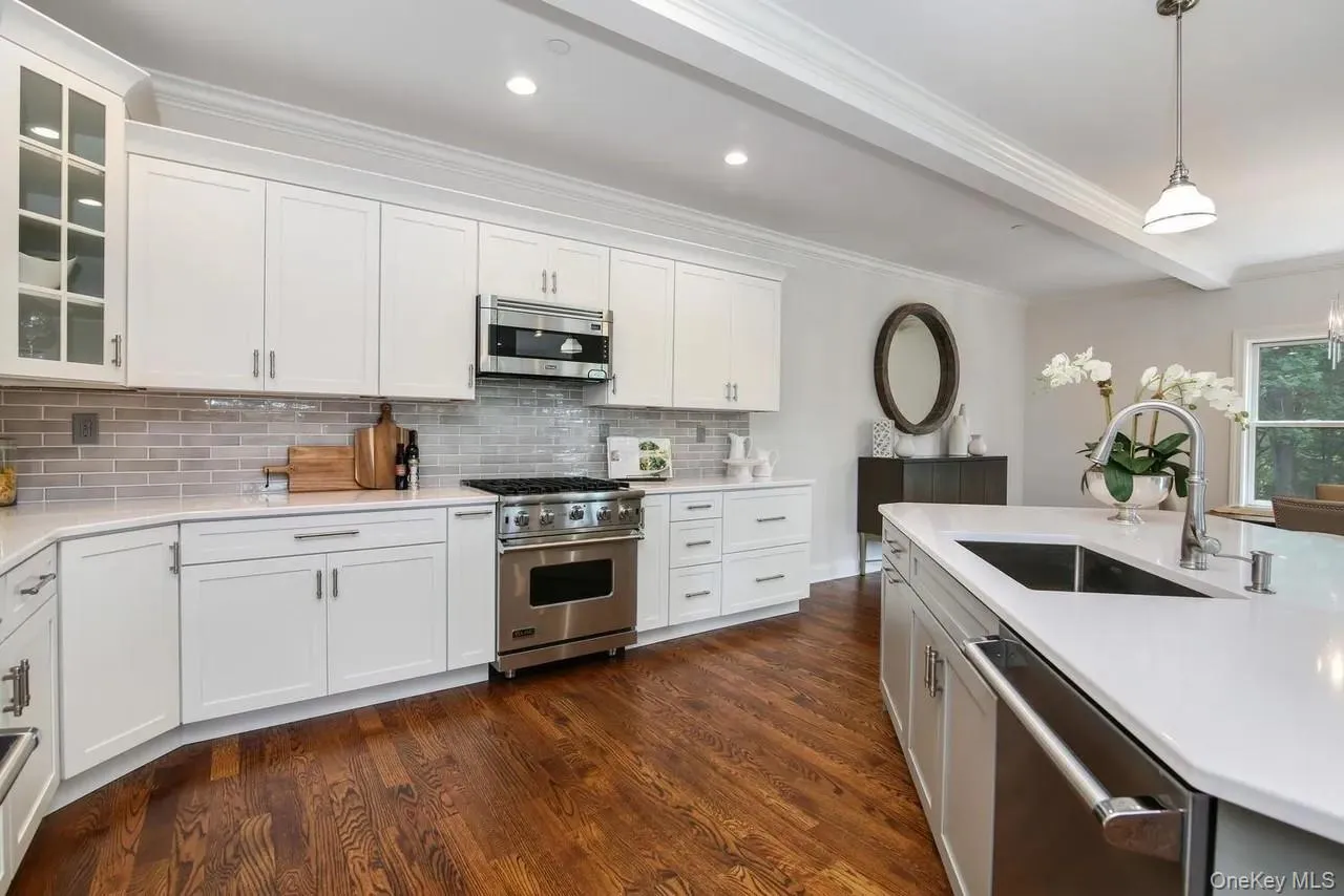 Kitchen with stainless steel appliances, white cabinets, decorative light fixtures, ornamental molding, and dark wood finished floors Kitchen with stainless steel appliances, white cabinets, decorative light fixtures, ornamental molding, and dark wood finished floors