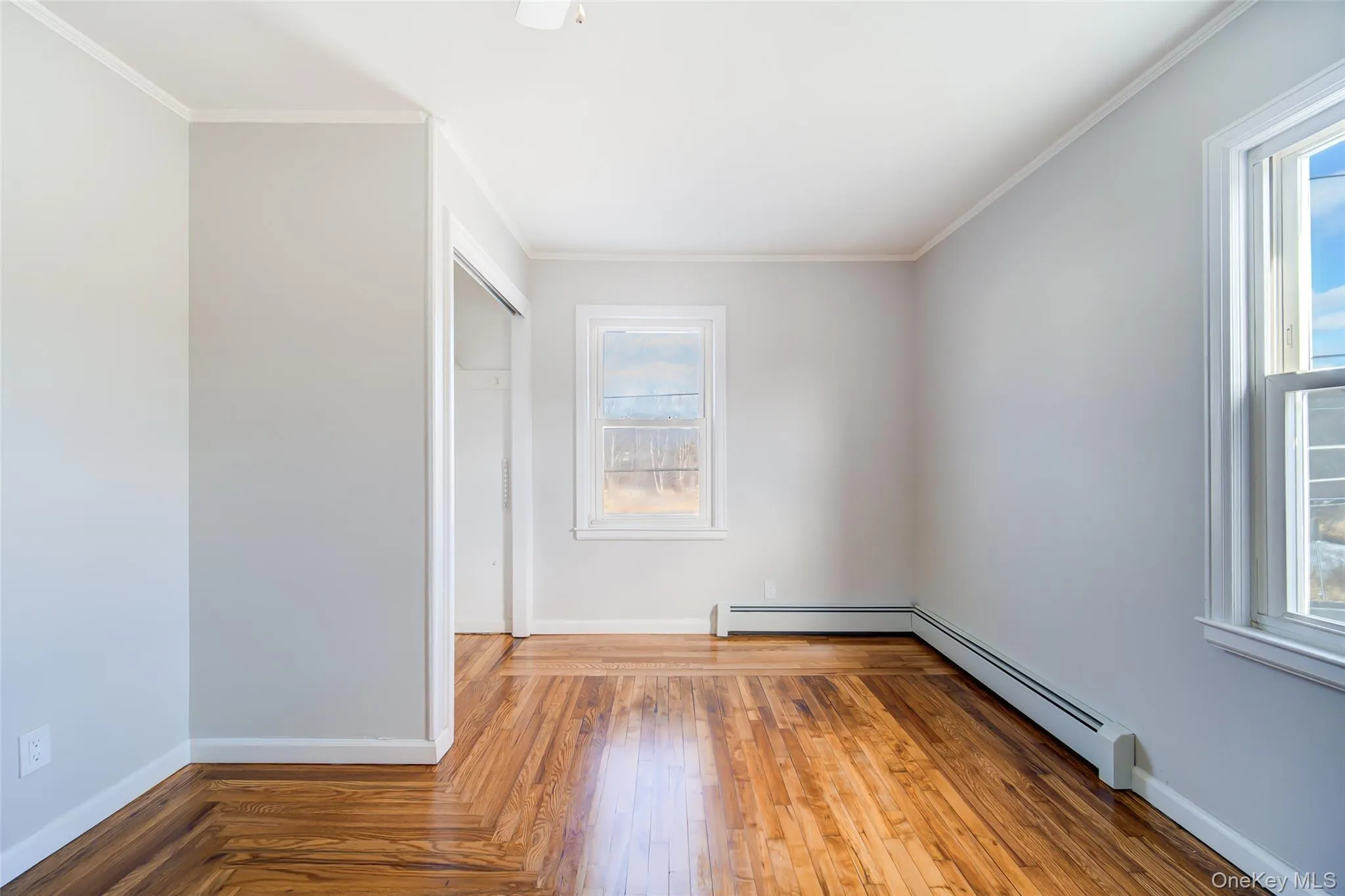 Bedroom featuring a baseboard radiator, light wood-style floors, and crown molding Bedroom featuring a baseboard radiator, light wood-style floors, and crown molding