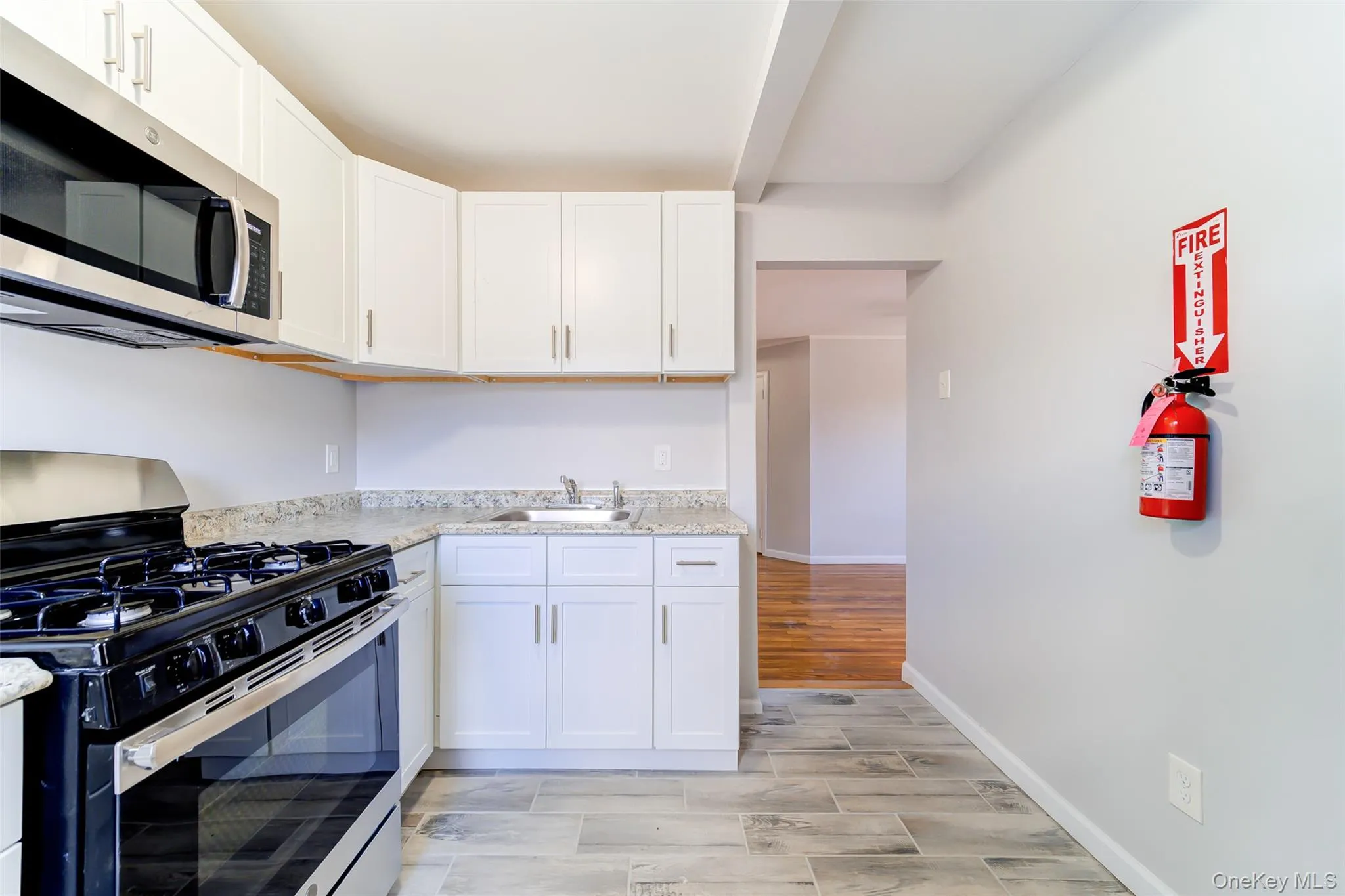 Kitchen featuring stainless steel appliances, white cabinetry, light stone countertops, and wood tiled floors Kitchen featuring stainless steel appliances, white cabinetry, light stone countertops, and wood tiled floors