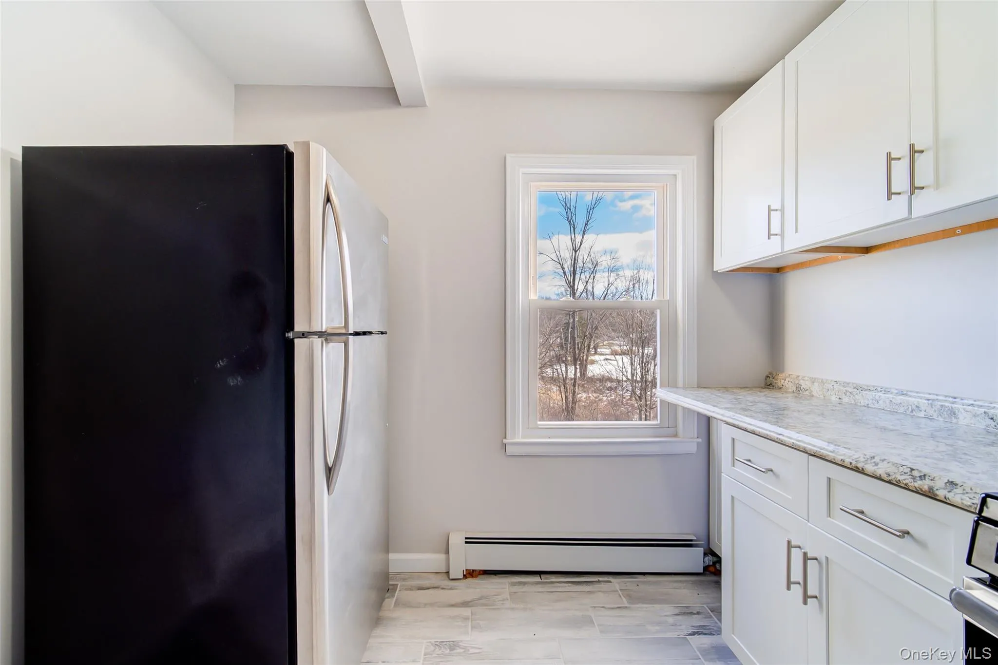 Kitchen featuring freestanding refrigerator, white cabinets, and baseboard heating Kitchen featuring freestanding refrigerator, white cabinets, and baseboard heating