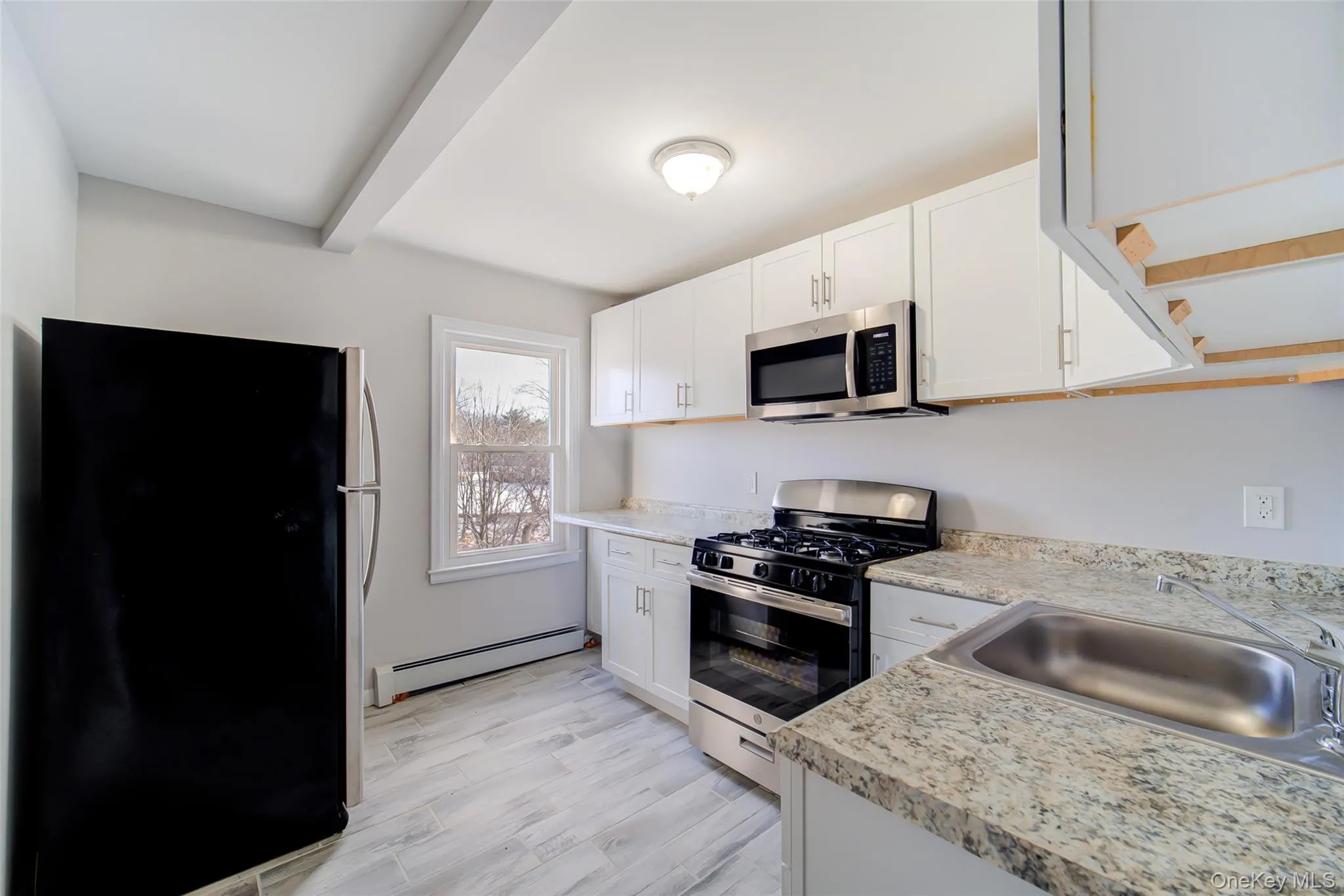 Kitchen featuring stainless steel appliances, light countertops, white cabinets, a baseboard radiator, and beamed ceiling Kitchen featuring stainless steel appliances, light countertops, white cabinets, a baseboard radiator, and beamed ceiling