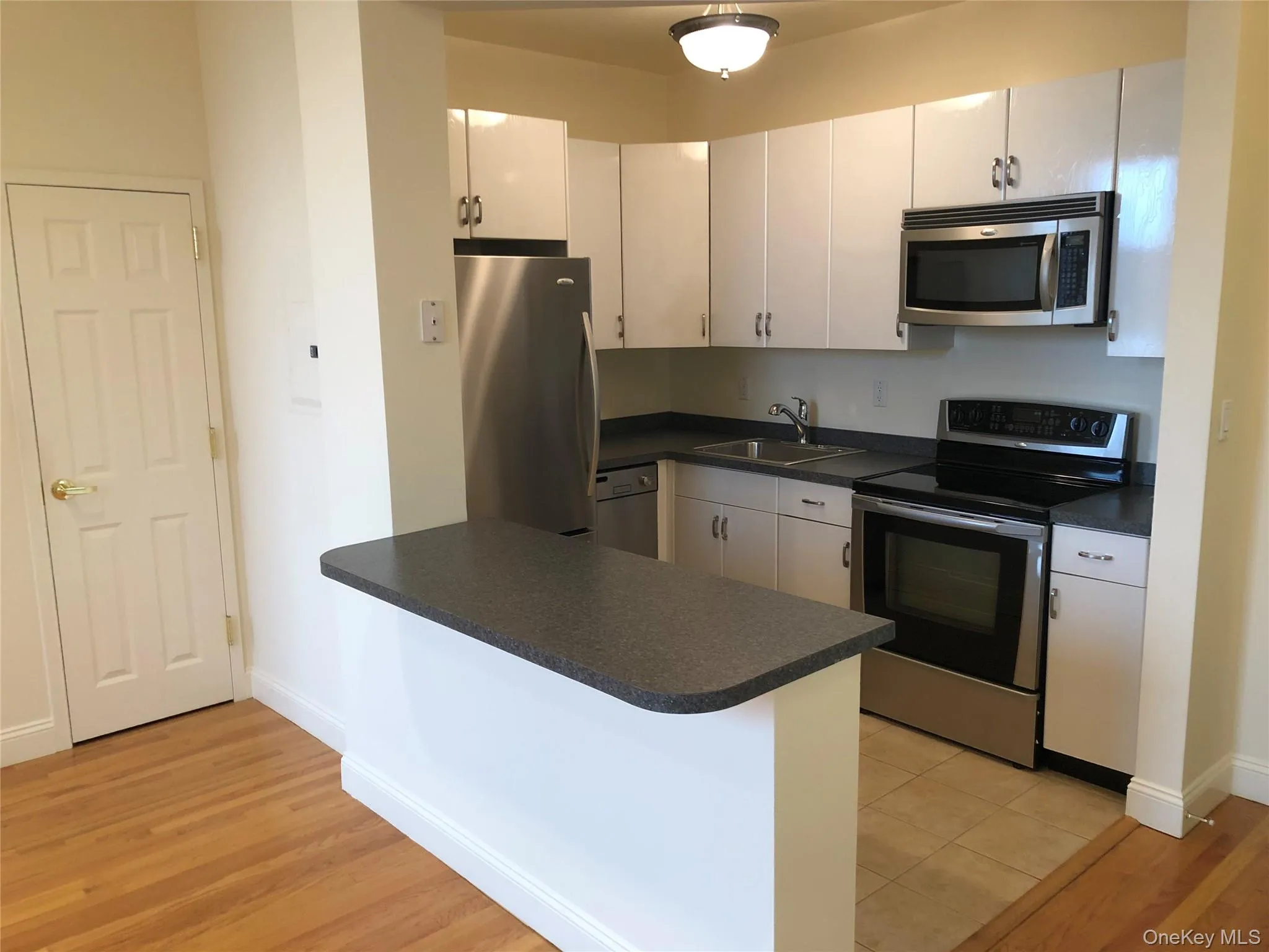 Kitchen featuring stainless steel appliances, dark countertops, light wood-style floors, and white cabinets Kitchen featuring stainless steel appliances, dark countertops, light wood-style floors, and white cabinets