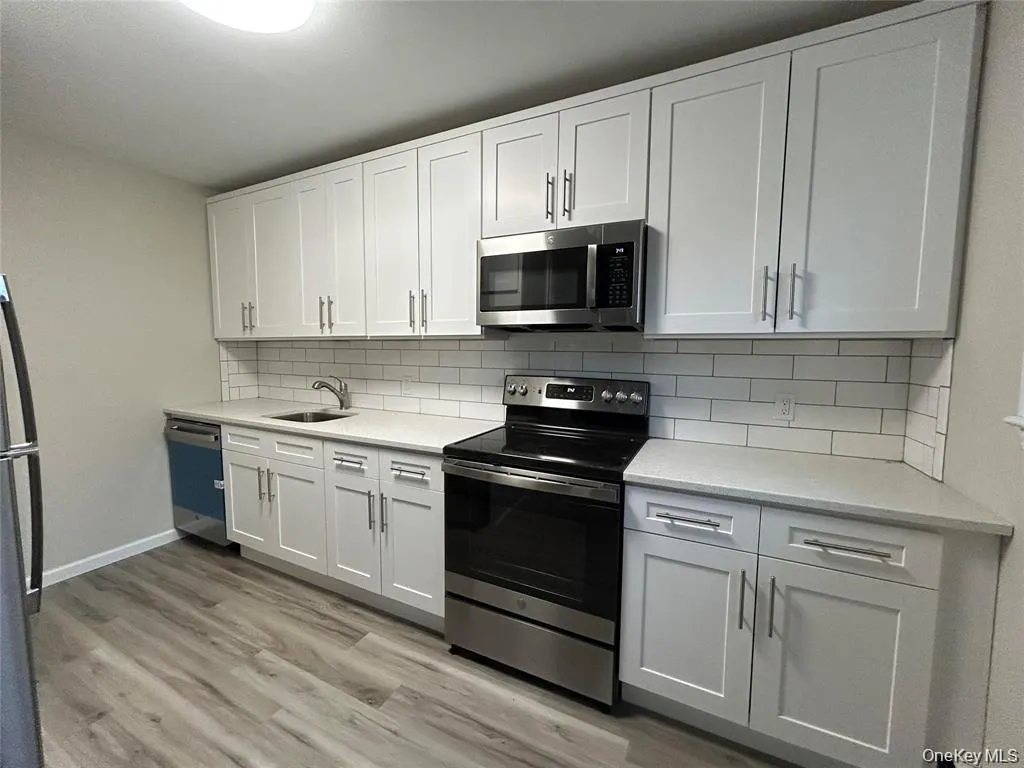 Kitchen featuring appliances with stainless steel finishes, light stone countertops, white cabinetry, light wood finished floors, and backsplash Kitchen featuring appliances with stainless steel finishes, light stone countertops, white cabinetry, light wood finished floors, and backsplash