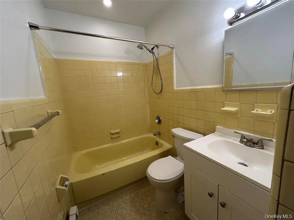 Bathroom with tile walls, vanity, shower combination, wainscoting, and a baseboard heating unit Bathroom with tile walls, vanity, shower combination, wainscoting, and a baseboard heating unit