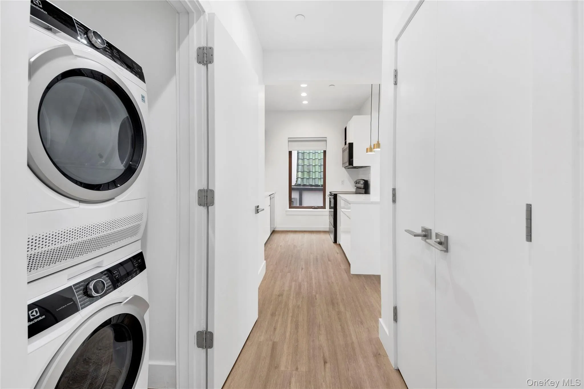 Laundry area featuring light wood-style floors, stacked washer / dryer, and recessed lighting Laundry area featuring light wood-style floors, stacked washer / dryer, and recessed lighting