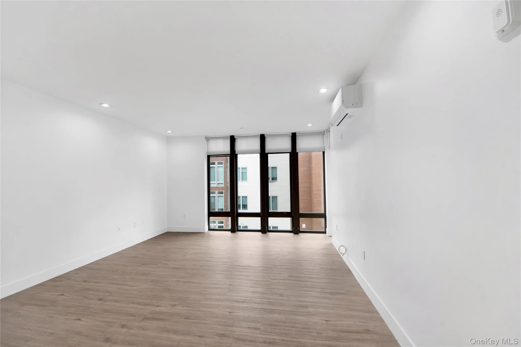 Empty room featuring light wood finished floors, floor to ceiling windows, recessed lighting, and a wall mounted AC Empty room featuring light wood finished floors, floor to ceiling windows, recessed lighting, and a wall mounted AC