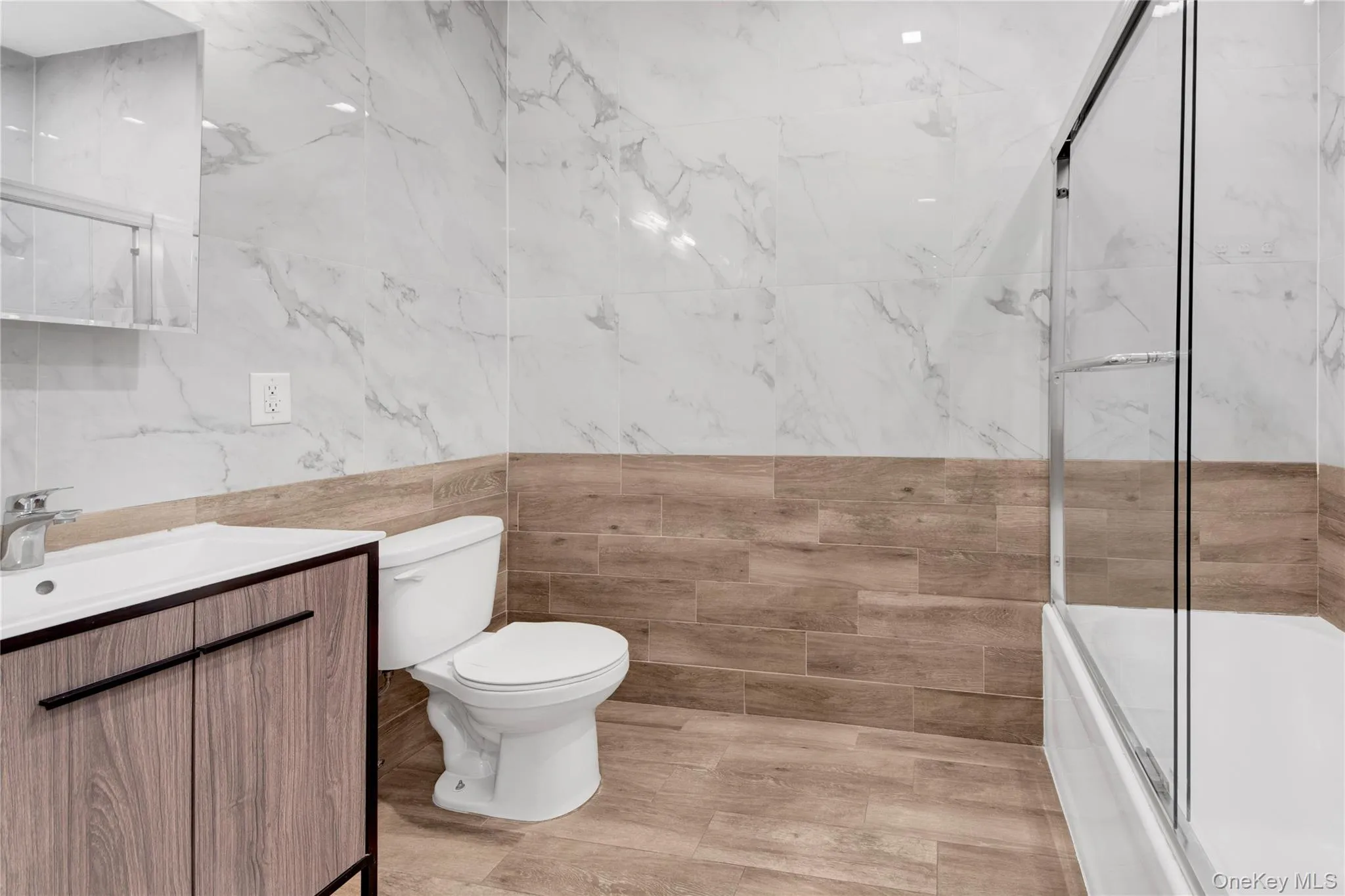 Bathroom featuring vanity, tile walls, and combined bath / shower with glass door Bathroom featuring vanity, tile walls, and combined bath / shower with glass door