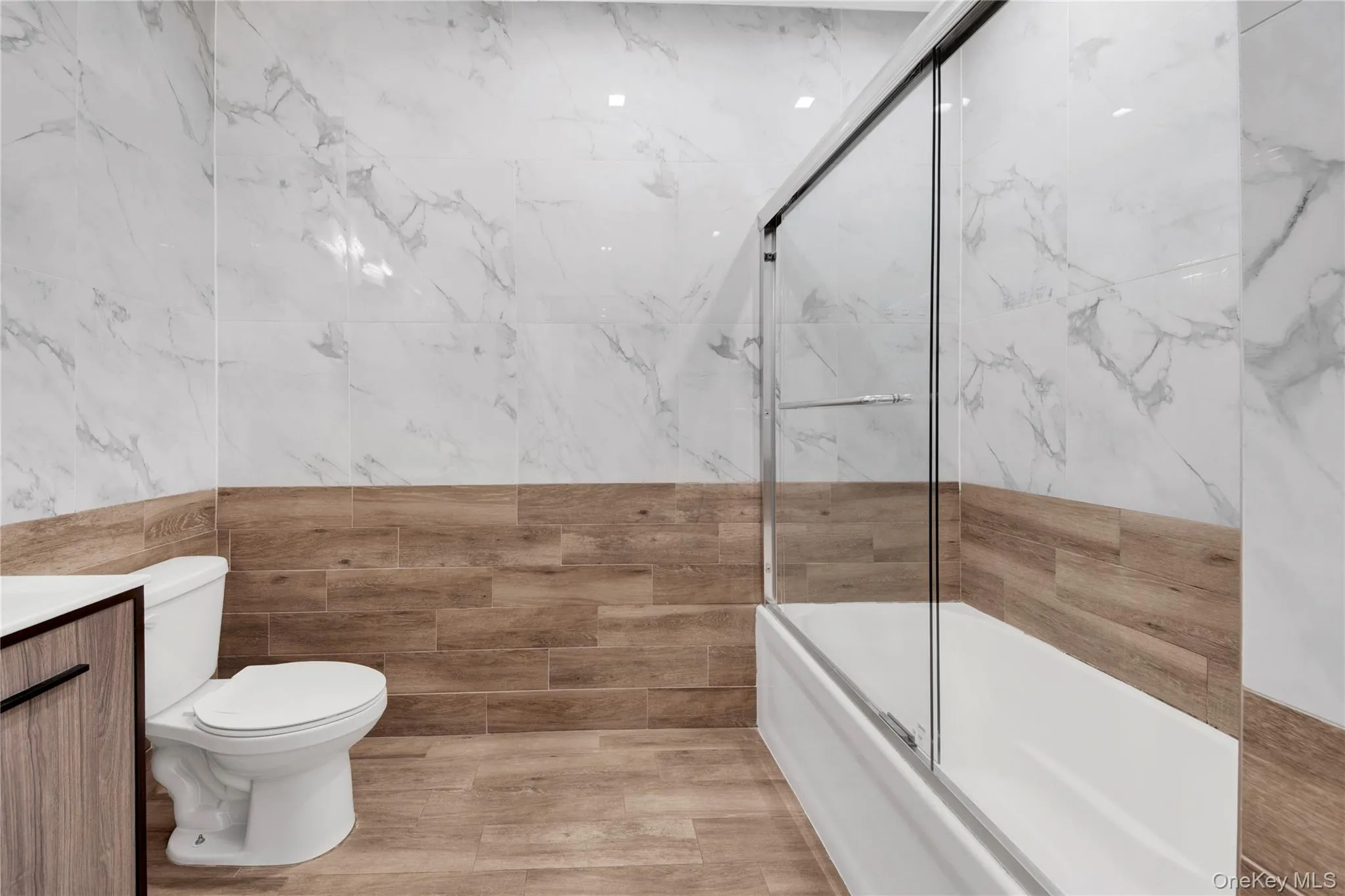 Full bathroom with combined bath / shower with glass door, vanity, and tile walls Full bathroom with combined bath / shower with glass door, vanity, and tile walls