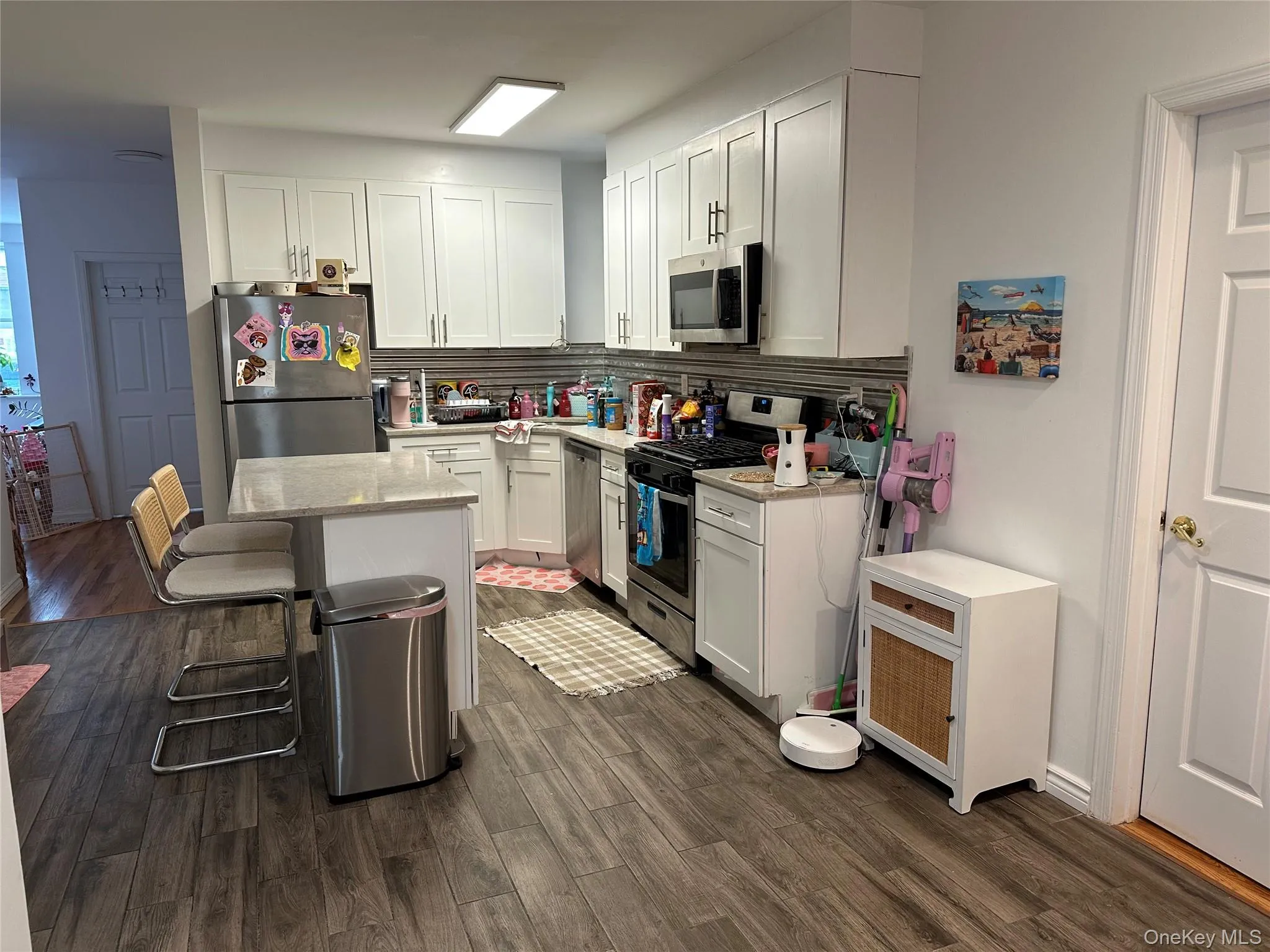 Kitchen featuring a kitchen breakfast bar, appliances with stainless steel finishes, white cabinetry, light stone countertops, and a kitchen island Kitchen featuring a kitchen breakfast bar, appliances with stainless steel finishes, white cabinetry, light stone countertops, and a kitchen island
