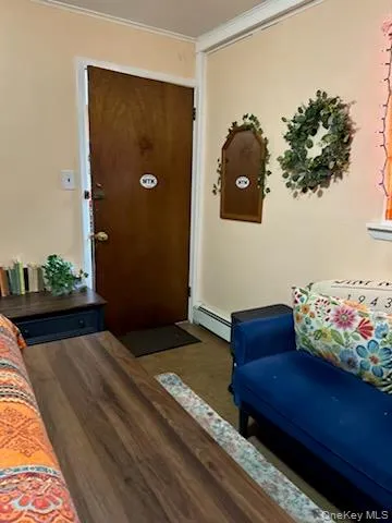 Living area with dark wood-style flooring, crown molding, and a baseboard heating unit Living area with dark wood-style flooring, crown molding, and a baseboard heating unit