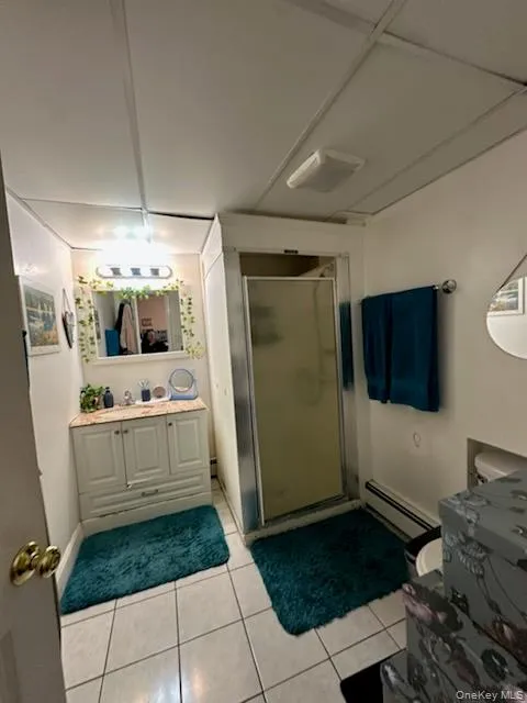 Full bath with a stall shower, vanity, light tile patterned flooring, and baseboard heating Full bath with a stall shower, vanity, light tile patterned flooring, and baseboard heating