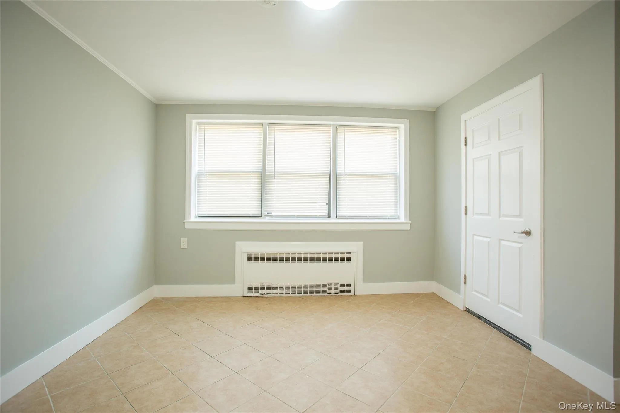 Unfurnished room with radiator heating unit, plenty of natural light, light tile patterned floors, and crown molding Unfurnished room with radiator heating unit, plenty of natural light, light tile patterned floors, and crown molding