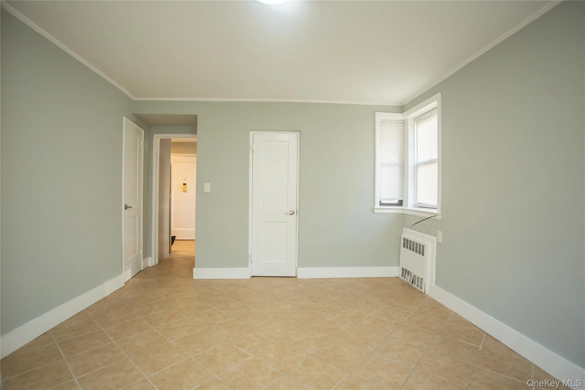 Spare room with radiator heating unit, crown molding, light tile patterned floors, and baseboards Spare room with radiator heating unit, crown molding, light tile patterned floors, and baseboards