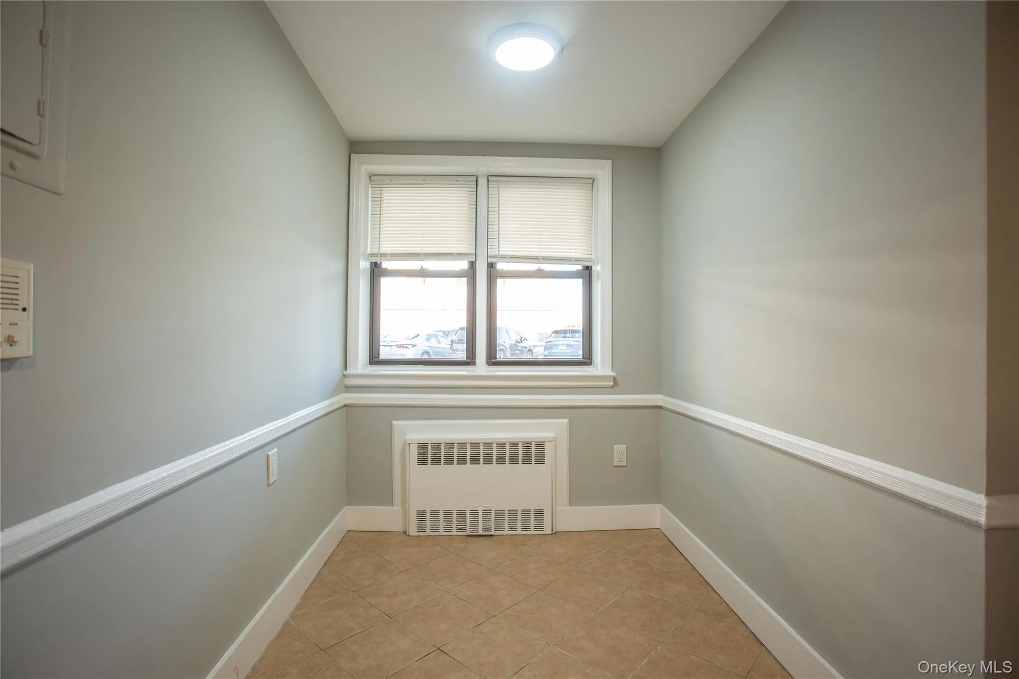 Empty room with radiator heating unit, baseboards, and light tile patterned flooring Empty room with radiator heating unit, baseboards, and light tile patterned flooring