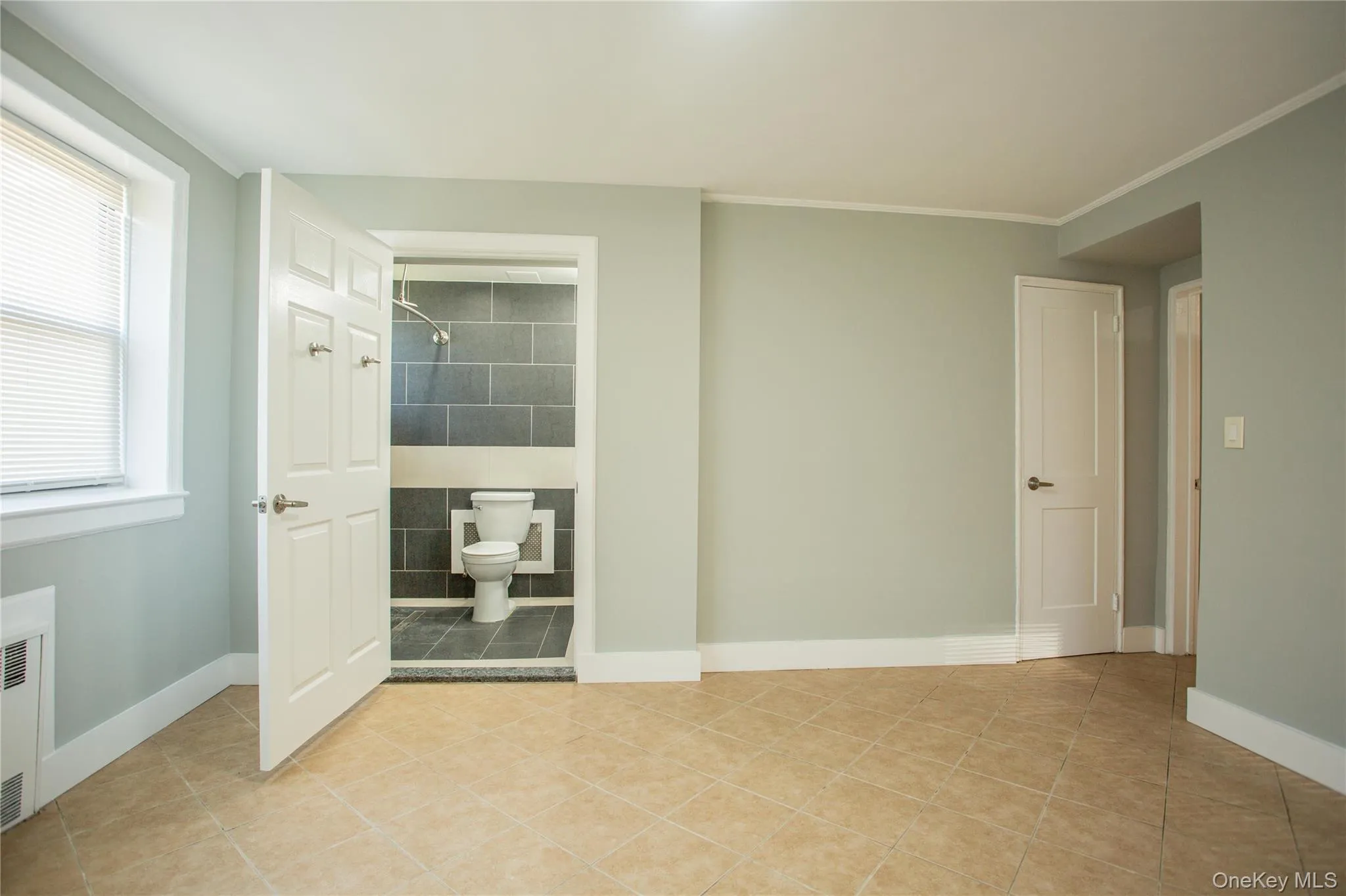 Empty room featuring light tile patterned floors, ornamental molding, baseboards, and radiator Empty room featuring light tile patterned floors, ornamental molding, baseboards, and radiator
