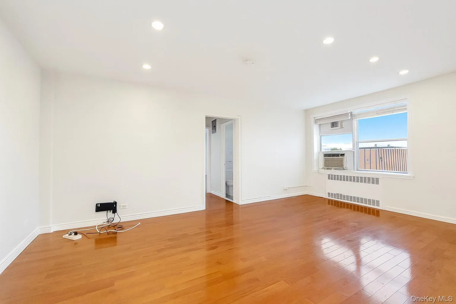 Empty room featuring recessed lighting, light wood-type flooring, and radiator heating unit Empty room featuring recessed lighting, light wood-type flooring, and radiator heating unit