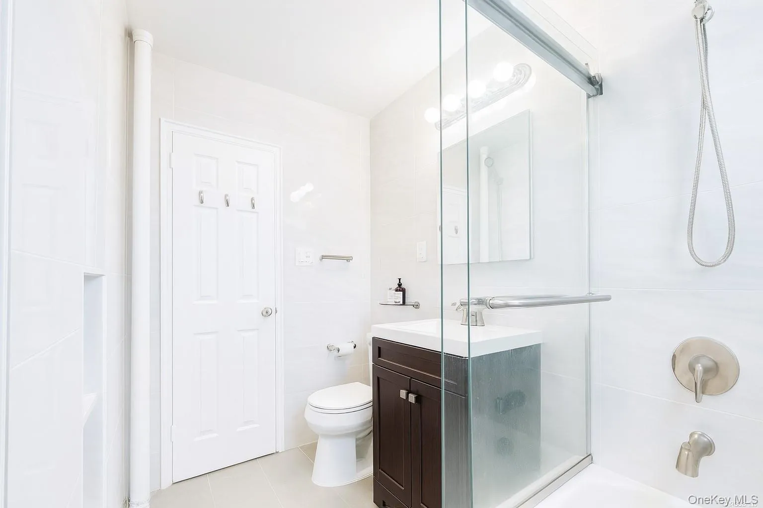 Bathroom featuring vanity, shower / bath combination with glass door, light tile patterned floors, and tile walls Bathroom featuring vanity, shower / bath combination with glass door, light tile patterned floors, and tile walls