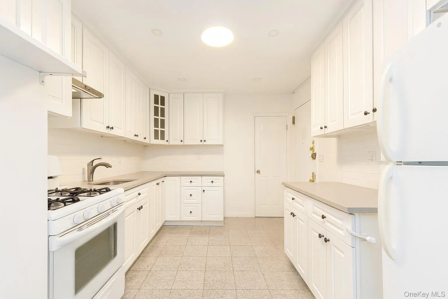 Kitchen with white appliances, light countertops, glass insert cabinets, and white cabinetry Kitchen with white appliances, light countertops, glass insert cabinets, and white cabinetry