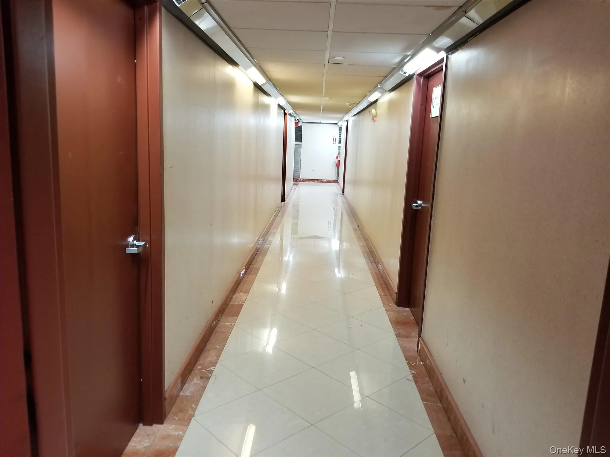 Corridor featuring light tile patterned flooring, a paneled ceiling, and inlaid floor details Corridor featuring light tile patterned flooring, a paneled ceiling, and inlaid floor details