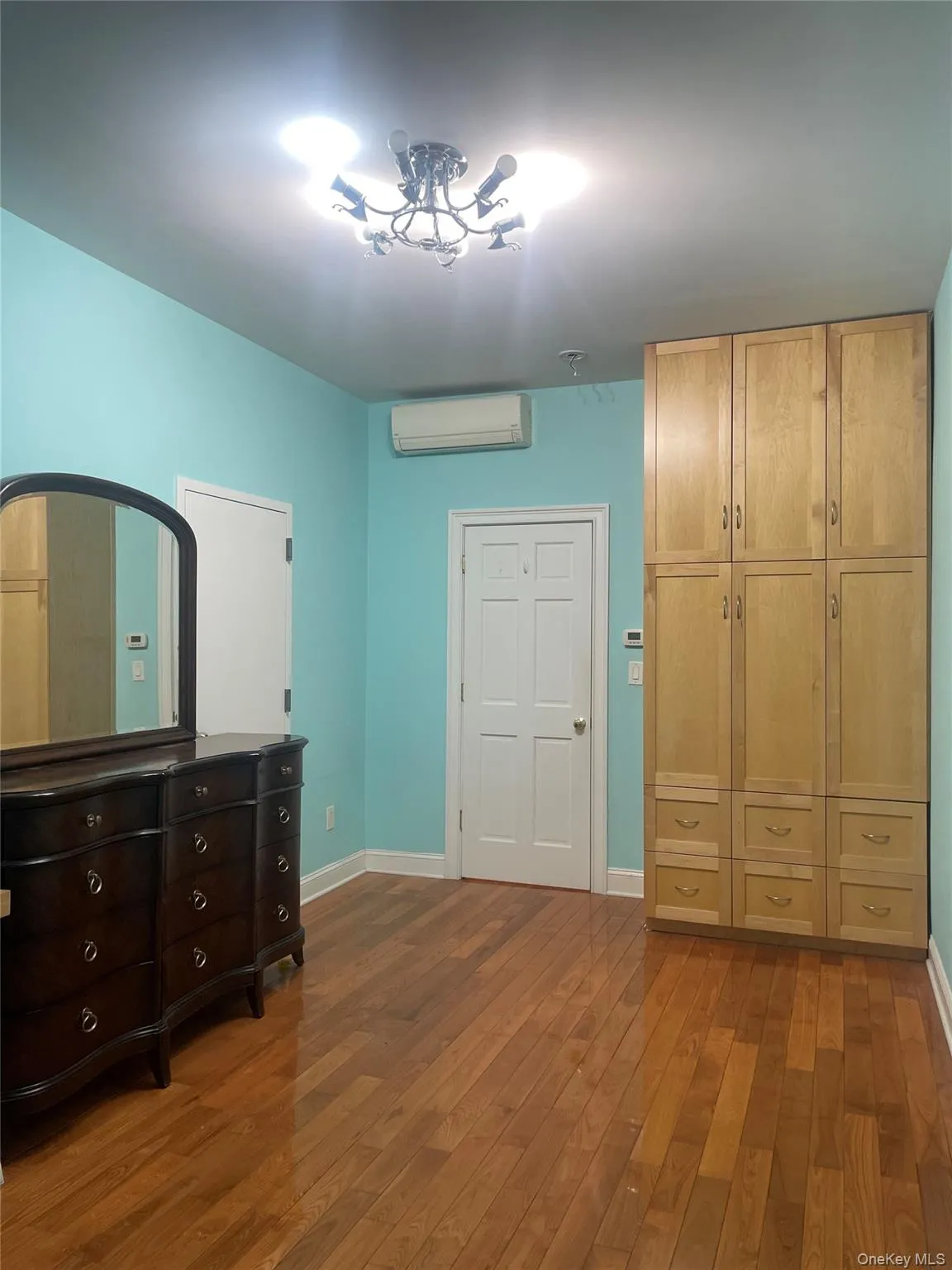 Unfurnished bedroom with dark wood-style flooring, a wall mounted air conditioner, and a closet Unfurnished bedroom with dark wood-style flooring, a wall mounted air conditioner, and a closet