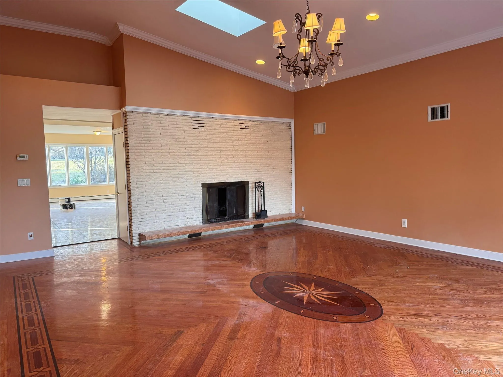 Unfurnished living room with crown molding, a fireplace, a skylight, a chandelier, and vaulted ceiling Unfurnished living room with crown molding, a fireplace, a skylight, a chandelier, and vaulted ceiling