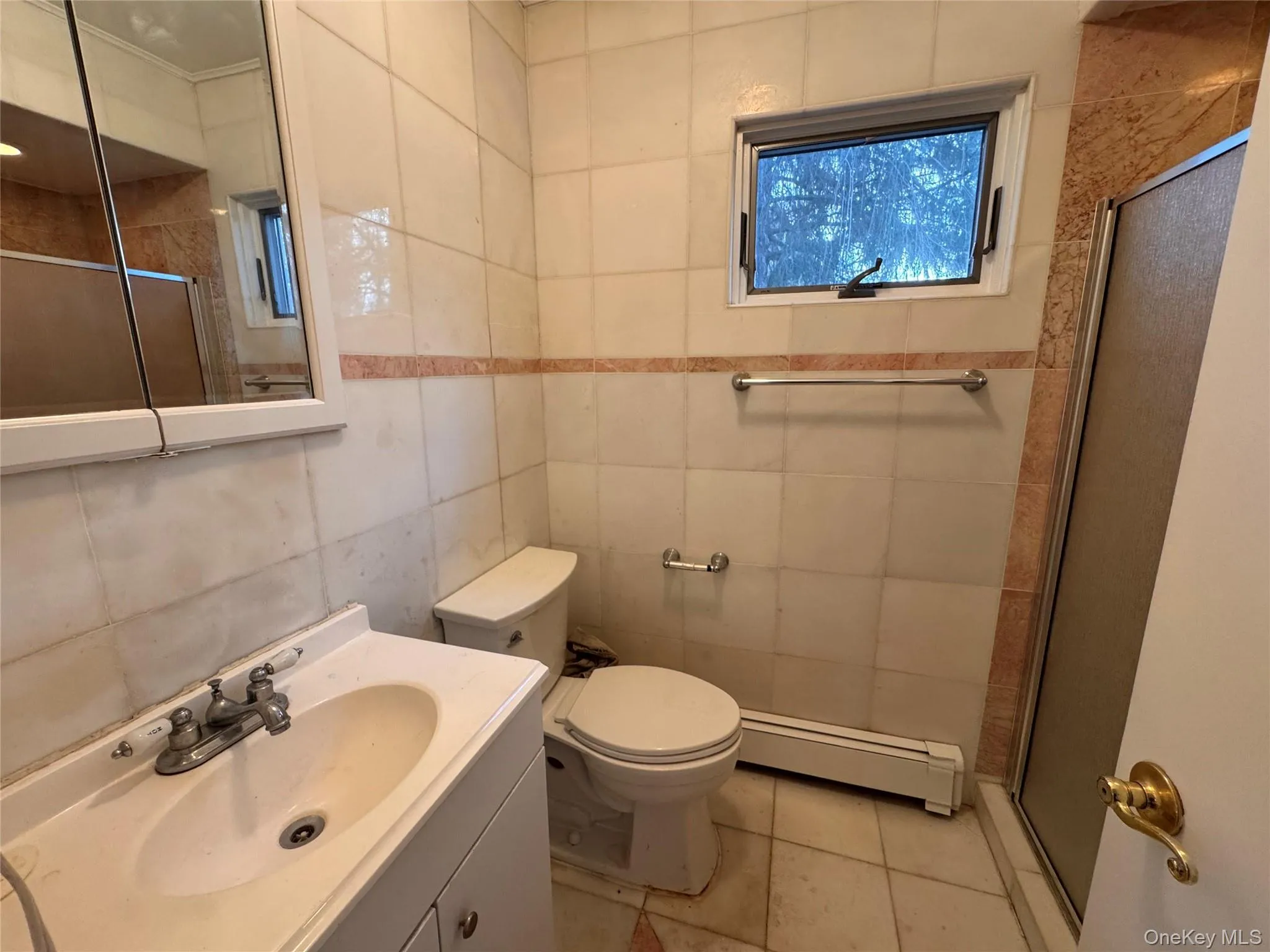 Full bath with a shower stall, vanity, baseboard heating, tile walls, and light tile patterned floors Full bath with a shower stall, vanity, baseboard heating, tile walls, and light tile patterned floors