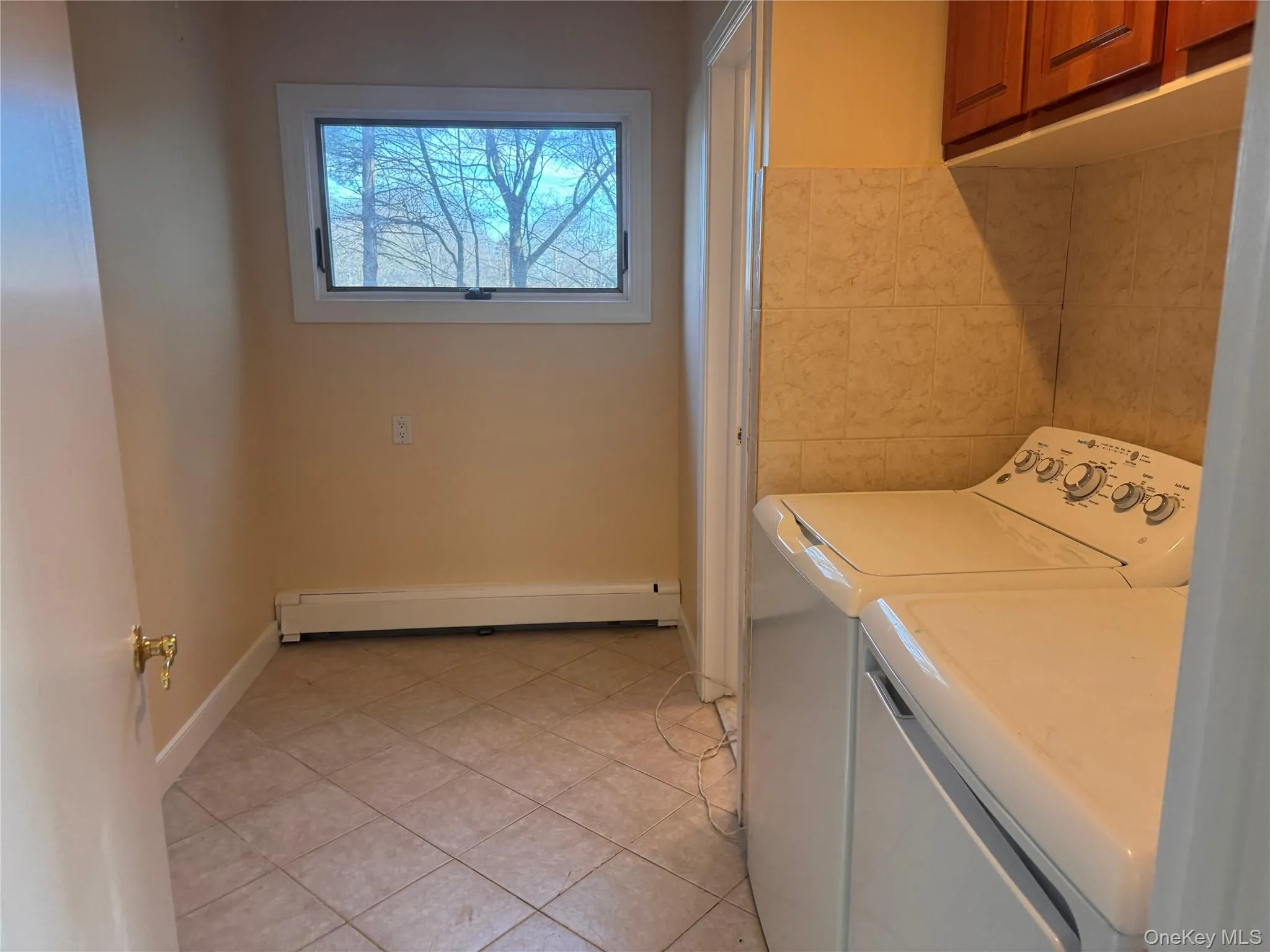 Washroom featuring cabinet space, baseboard heating, separate washer and dryer, and light tile patterned flooring Washroom featuring cabinet space, baseboard heating, separate washer and dryer, and light tile patterned flooring