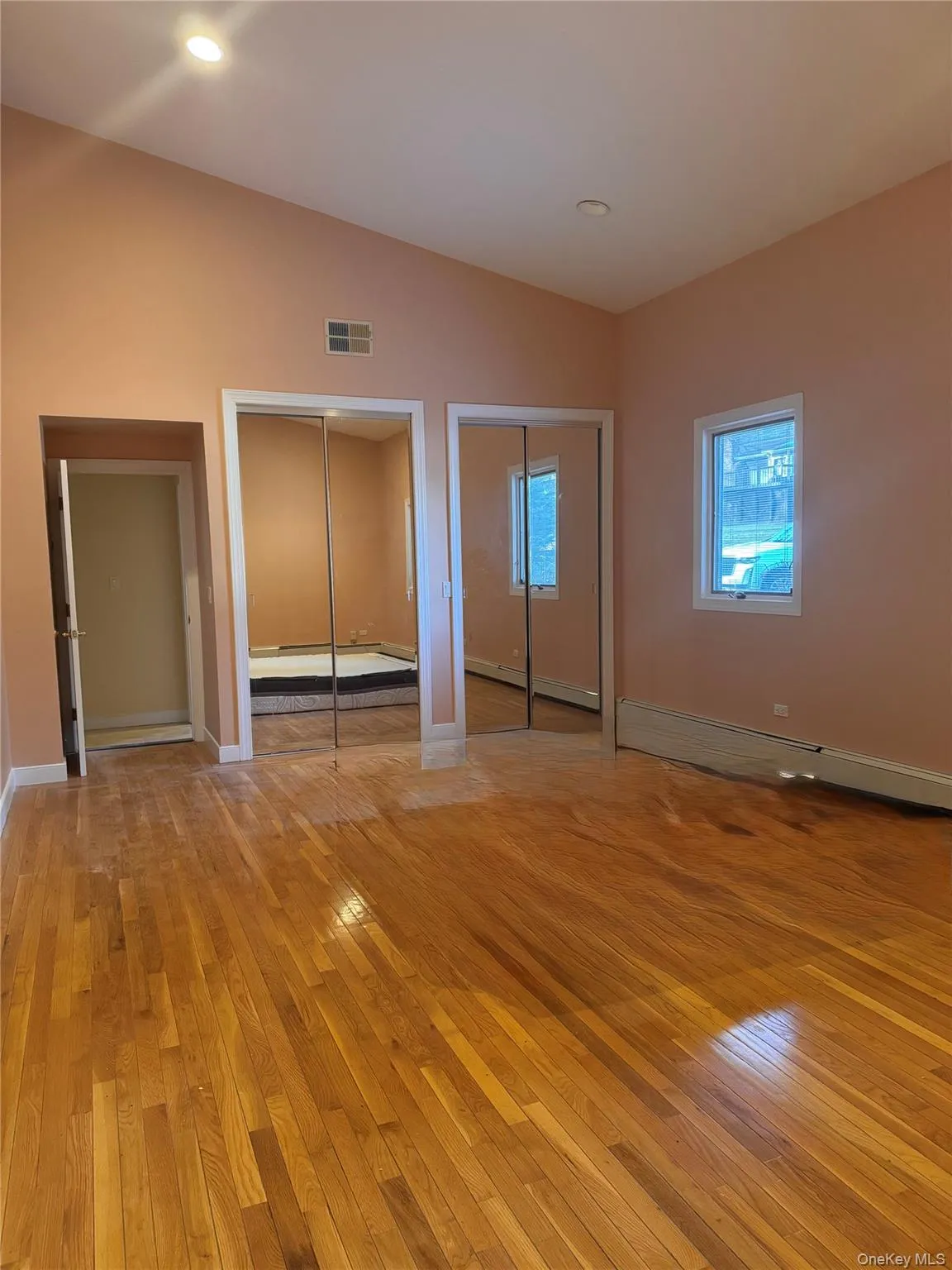 Unfurnished bedroom featuring two closets, lofted ceiling, light wood-style floors, a baseboard heating unit, and recessed lighting Unfurnished bedroom featuring two closets, lofted ceiling, light wood-style floors, a baseboard heating unit, and recessed lighting