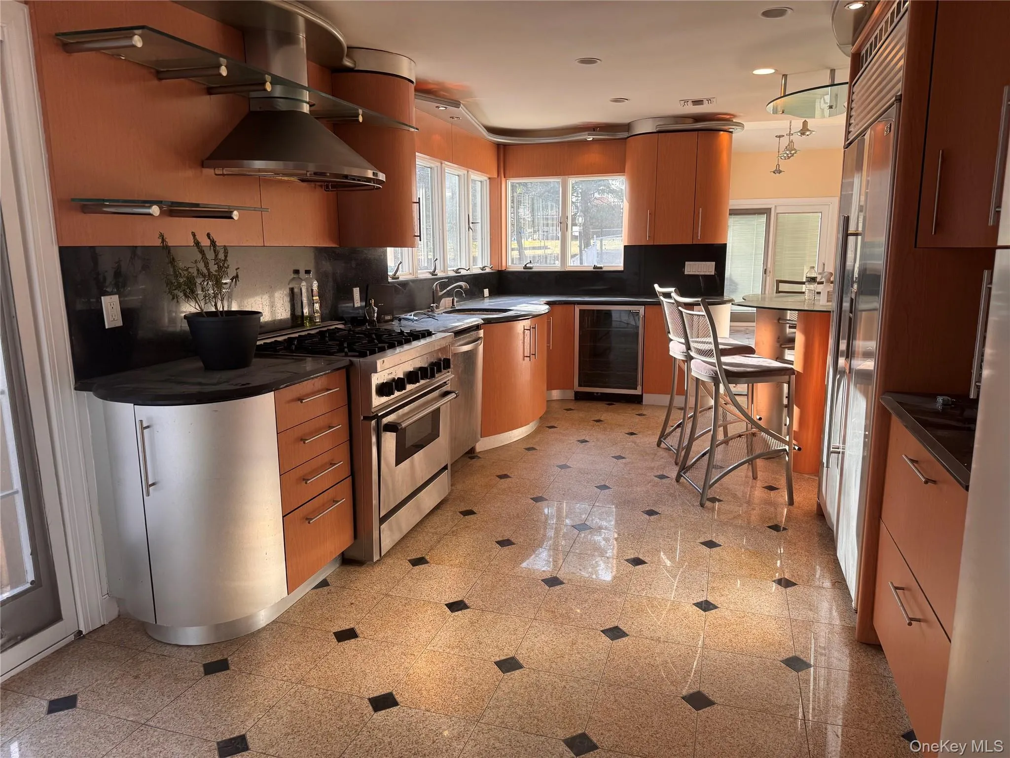 Kitchen featuring stainless steel appliances, beverage cooler, dark stone countertops, a kitchen breakfast bar, and modern cabinets Kitchen featuring stainless steel appliances, beverage cooler, dark stone countertops, a kitchen breakfast bar, and modern cabinets