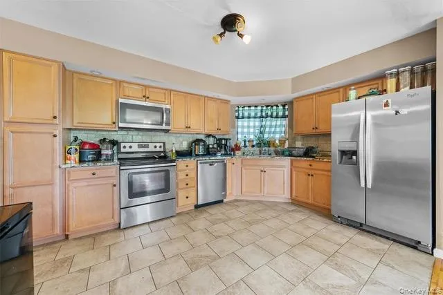 Kitchen featuring stainless steel appliances, light brown cabinets, backsplash, and dark stone counters Kitchen featuring stainless steel appliances, light brown cabinets, backsplash, and dark stone counters