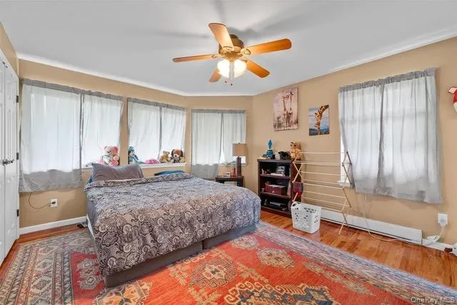 Bedroom with wood finished floors, multiple windows, ceiling fan, and a baseboard radiator Bedroom with wood finished floors, multiple windows, ceiling fan, and a baseboard radiator