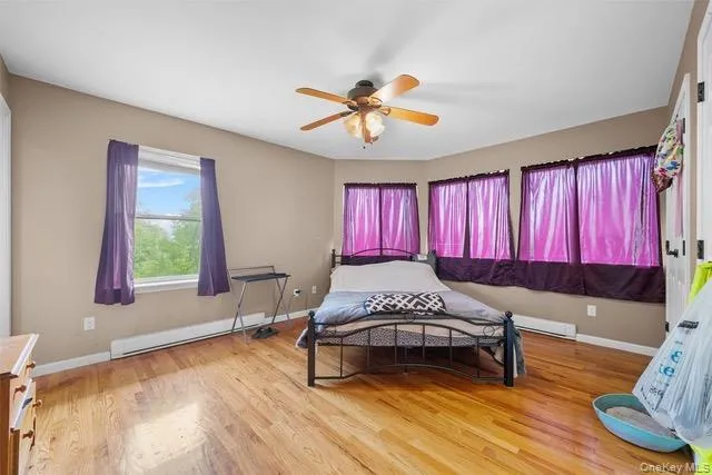 Bedroom featuring light wood-style floors, a baseboard heating unit, and a ceiling fan Bedroom featuring light wood-style floors, a baseboard heating unit, and a ceiling fan