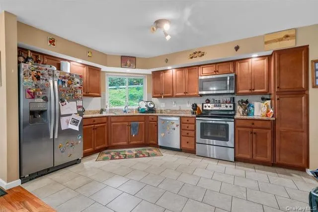 Kitchen with brown cabinets, appliances with stainless steel finishes, light tile patterned floors, and decorative backsplash Kitchen with brown cabinets, appliances with stainless steel finishes, light tile patterned floors, and decorative backsplash