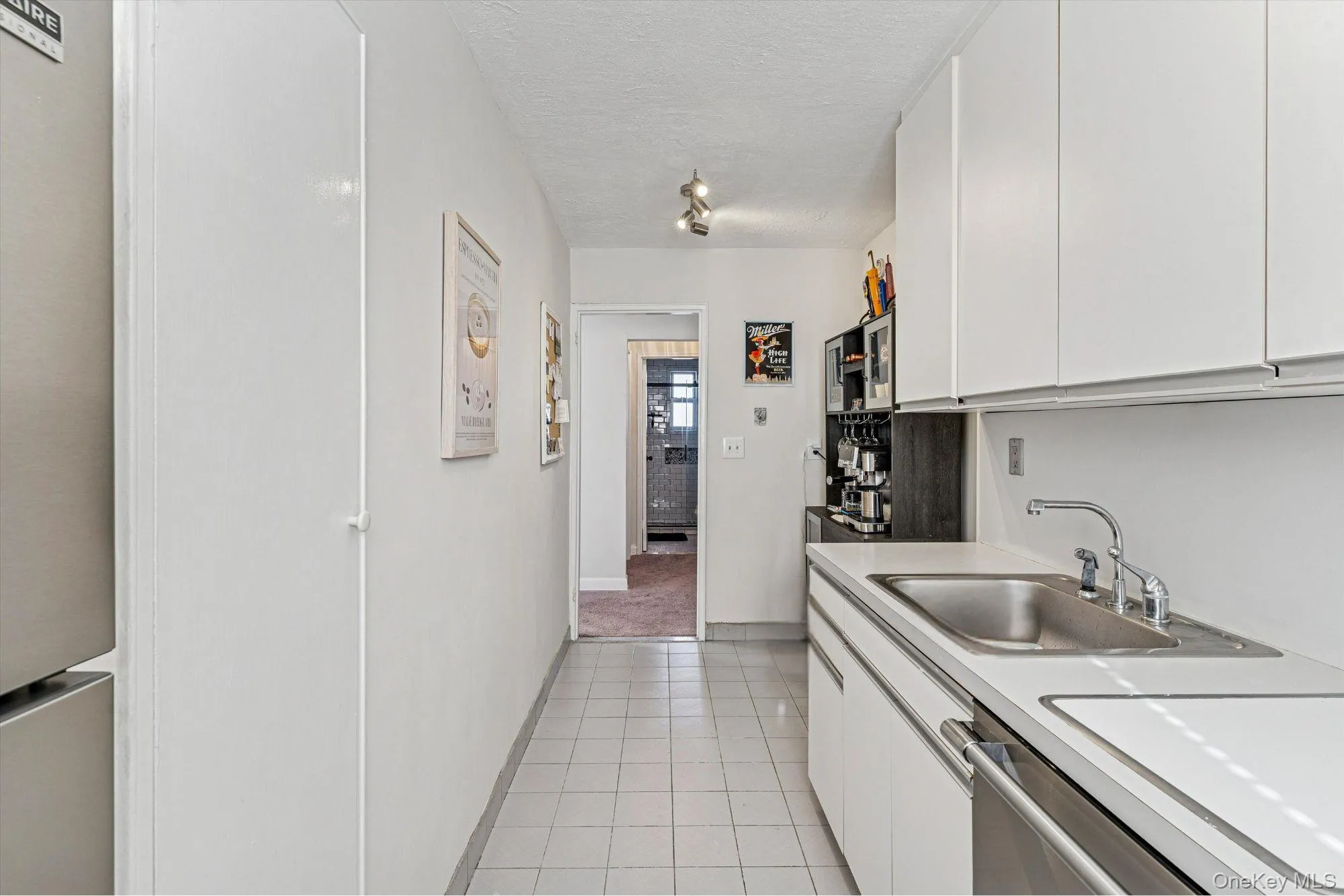 Kitchen featuring white cabinets, appliances with stainless steel finishes, light countertops, light tile patterned floors, and a textured ceiling Kitchen featuring white cabinets, appliances with stainless steel finishes, light countertops, light tile patterned floors, and a textured ceiling