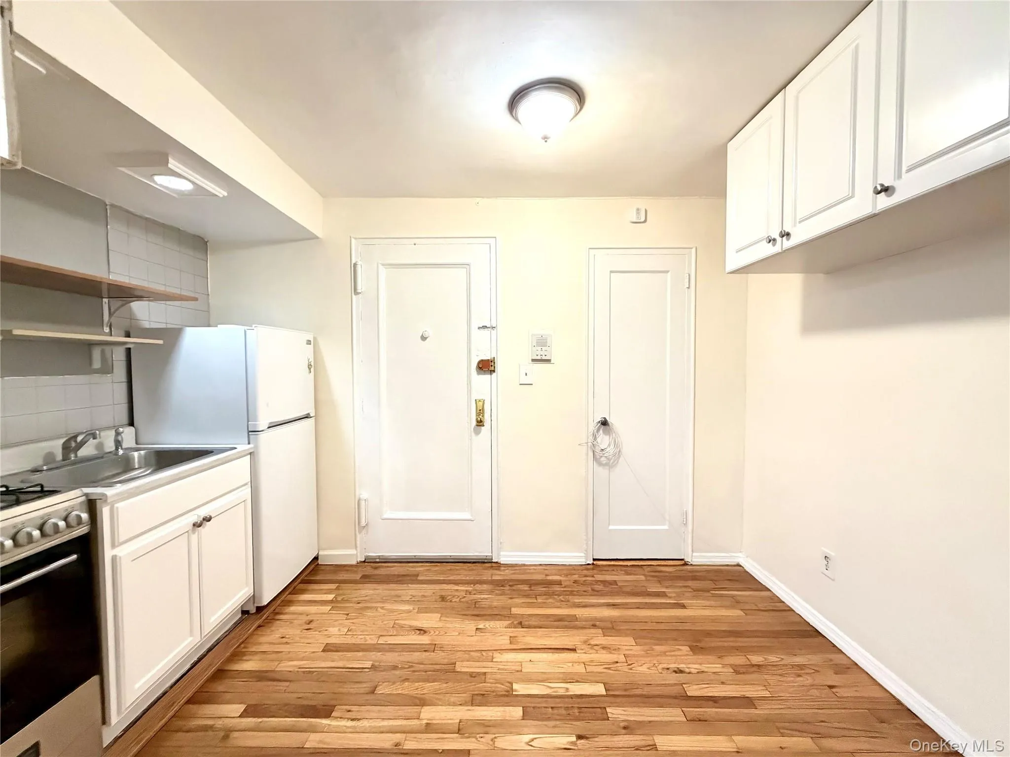 Kitchen with white cabinetry, open shelves, stainless steel range with gas cooktop, light wood finished floors, and freestanding refrigerator Kitchen with white cabinetry, open shelves, stainless steel range with gas cooktop, light wood finished floors, and freestanding refrigerator