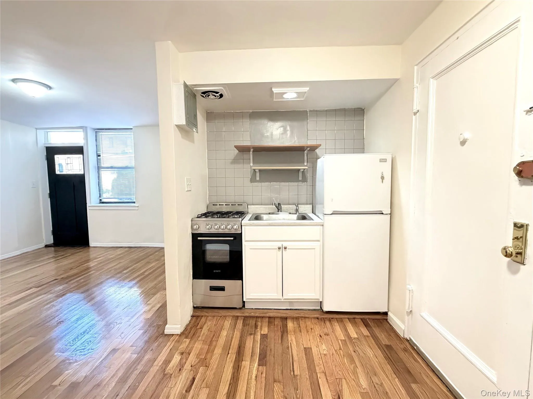 Kitchen featuring freestanding refrigerator, range with gas stovetop, tasteful backsplash, light wood-style floors, and white cabinets Kitchen featuring freestanding refrigerator, range with gas stovetop, tasteful backsplash, light wood-style floors, and white cabinets