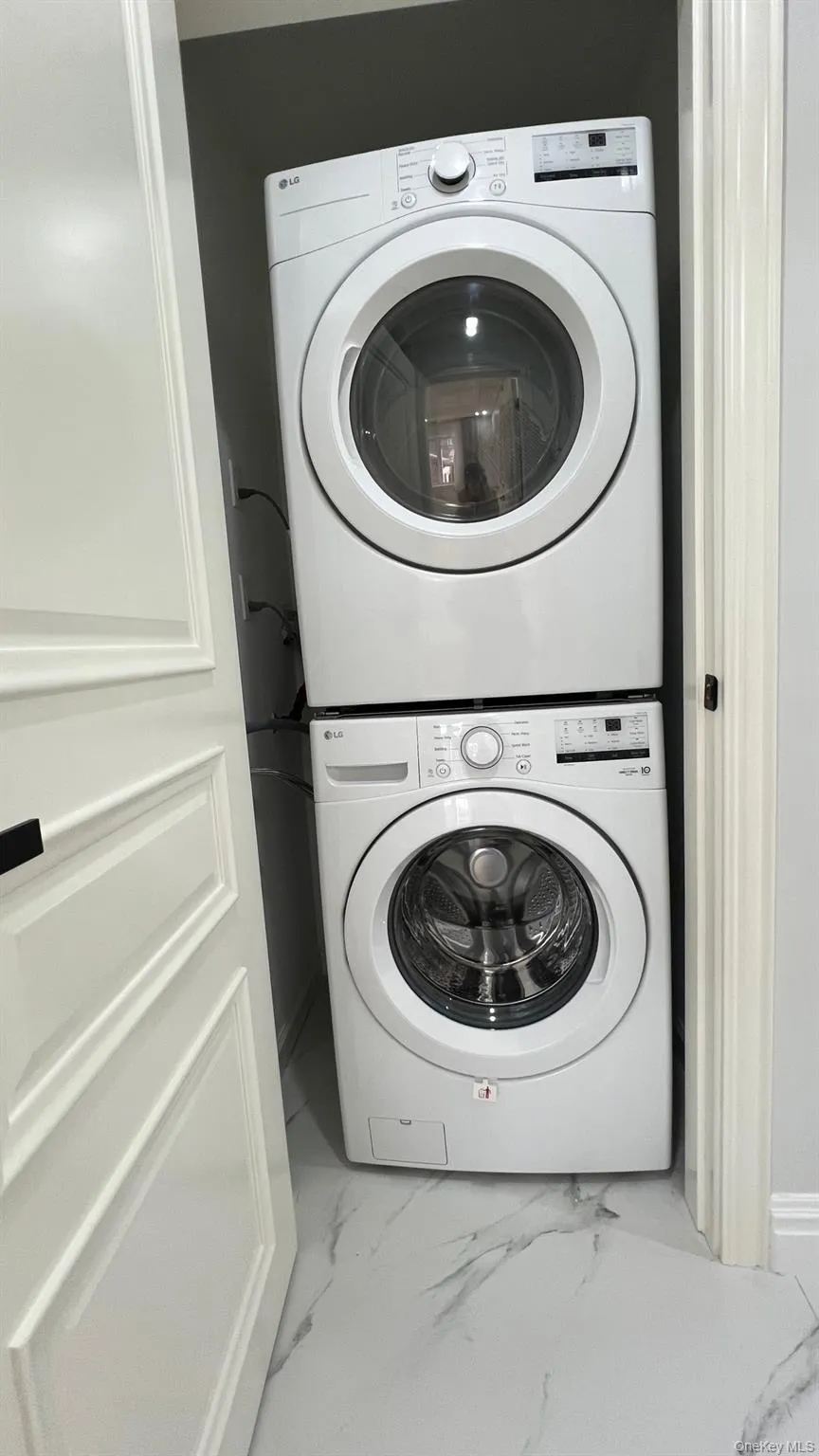 Washroom featuring marble look tiles and stacked washer and clothes dryer Washroom featuring marble look tiles and stacked washer and clothes dryer