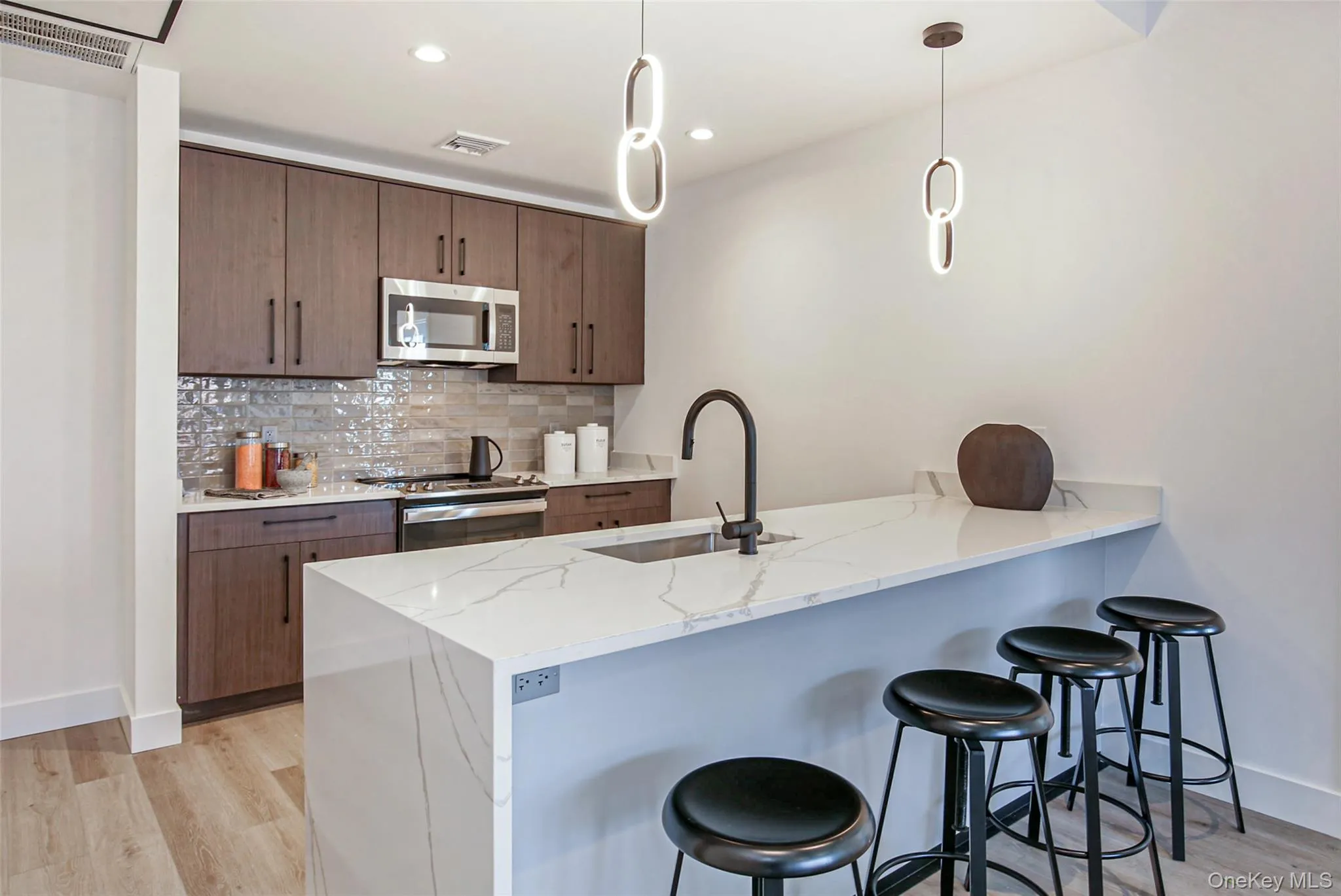 Kitchen featuring stainless steel appliances, light wood-type flooring, a peninsula, a breakfast bar, and tasteful backsplash Kitchen featuring stainless steel appliances, light wood-type flooring, a peninsula, a breakfast bar, and tasteful backsplash