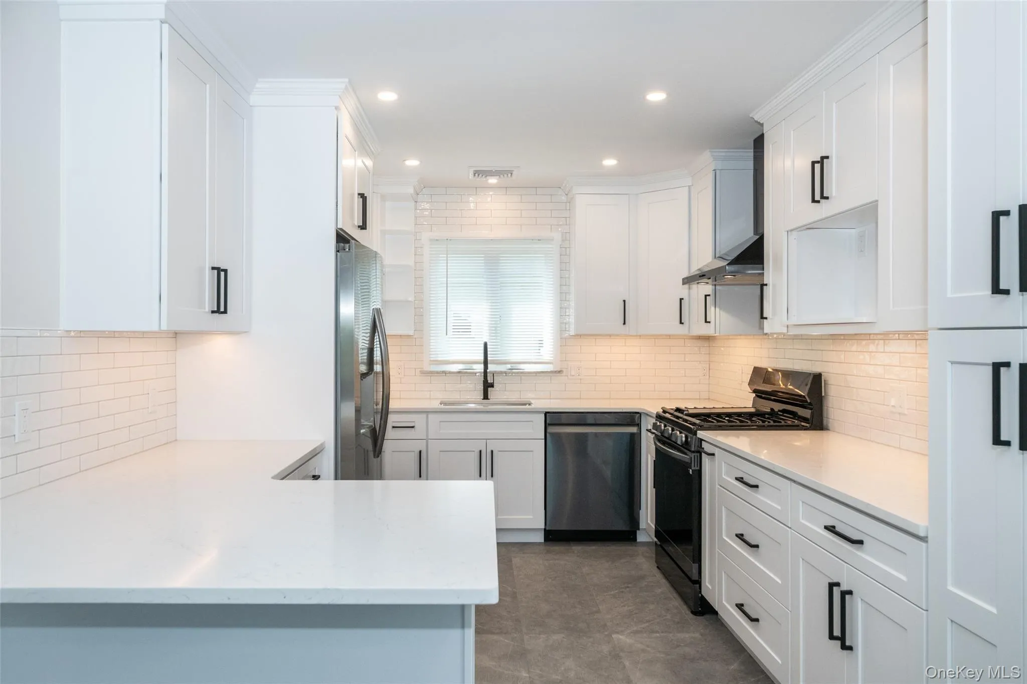 Kitchen with appliances with stainless steel finishes, white cabinetry, and wall chimney range hood Kitchen with appliances with stainless steel finishes, white cabinetry, and wall chimney range hood