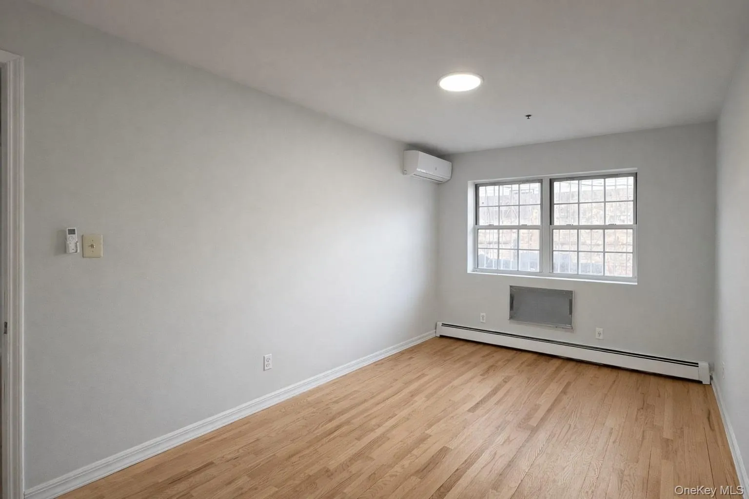 Spare room featuring a baseboard radiator, light wood-style floors, and a wall mounted AC Spare room featuring a baseboard radiator, light wood-style floors, and a wall mounted AC