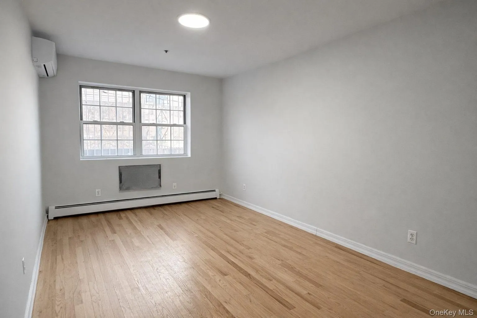 Empty room with baseboard heating, a wall unit AC, and light wood-type flooring Empty room with baseboard heating, a wall unit AC, and light wood-type flooring