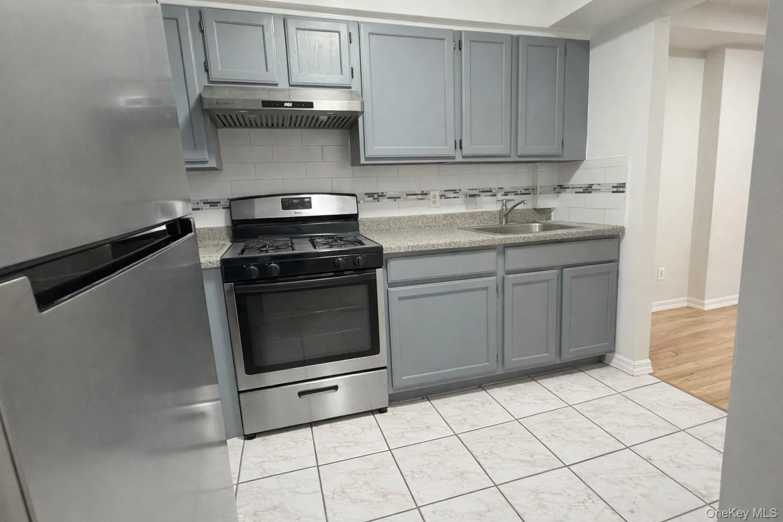 Kitchen with gray cabinetry, appliances with stainless steel finishes, backsplash, ventilation hood, and light countertops Kitchen with gray cabinetry, appliances with stainless steel finishes, backsplash, ventilation hood, and light countertops