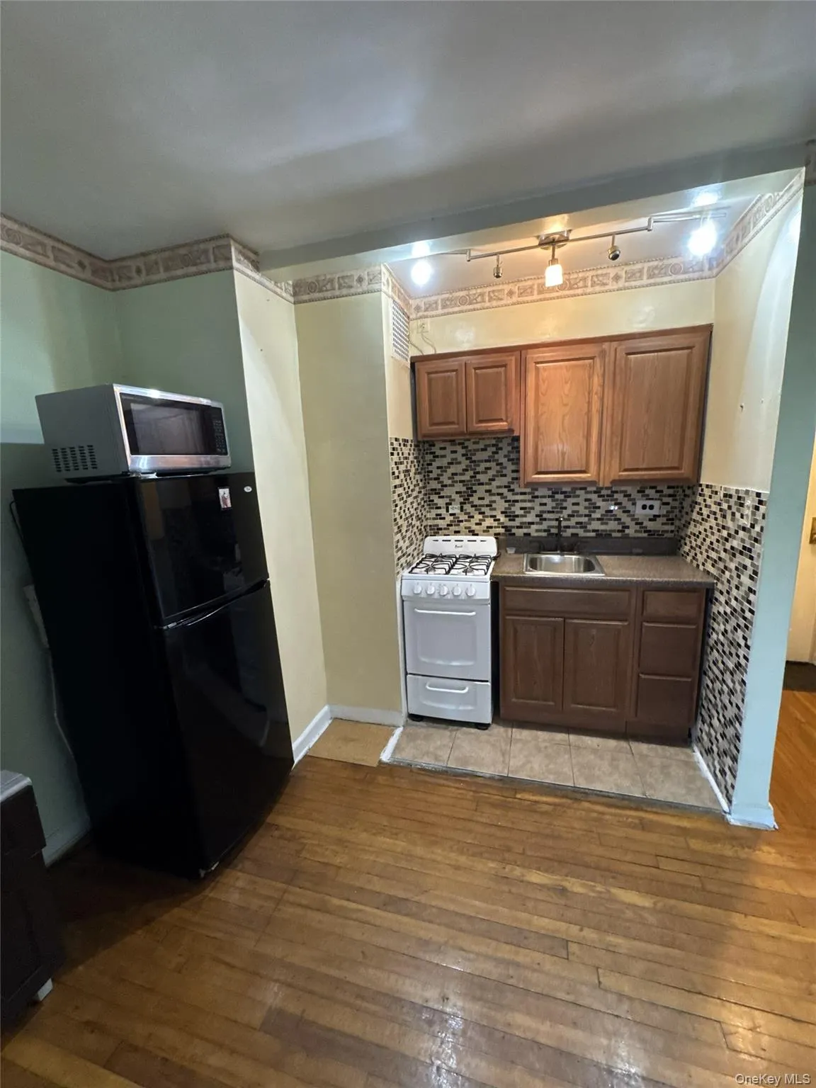 Kitchen with freestanding refrigerator, gas range gas stove, light wood-style flooring, stainless steel microwave, and decorative backsplash Kitchen with freestanding refrigerator, gas range gas stove, light wood-style flooring, stainless steel microwave, and decorative backsplash